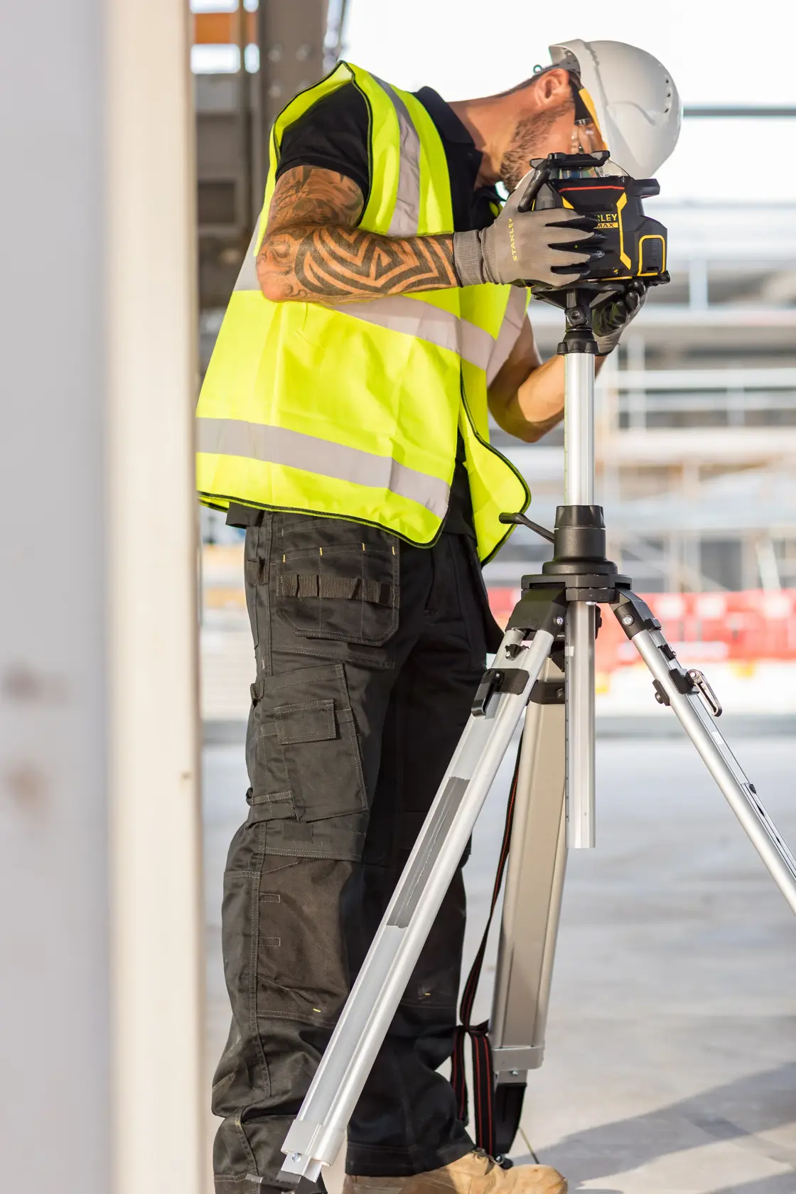STANLEY FMHT77224-1 laser level on tripod used by worker in safety vest and helmet on construction site.