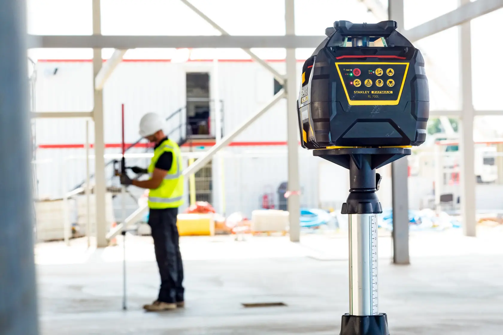 STANLEY FMHT77224-1 laser level on tripod at construction site with worker in background.