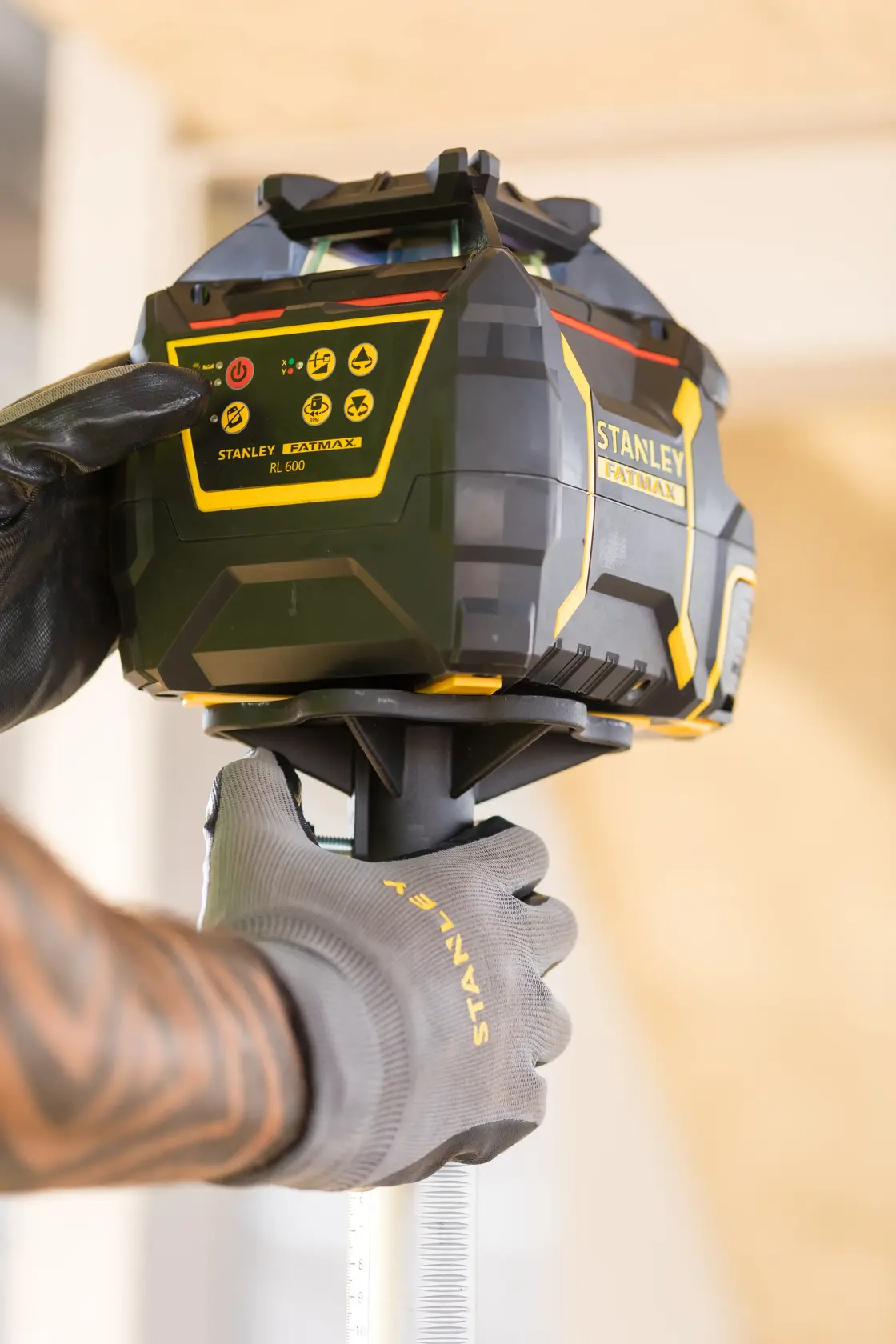 Photo of STANLEY FMHT77446-1 rotary laser level being operated by a gloved hand on a construction site.
