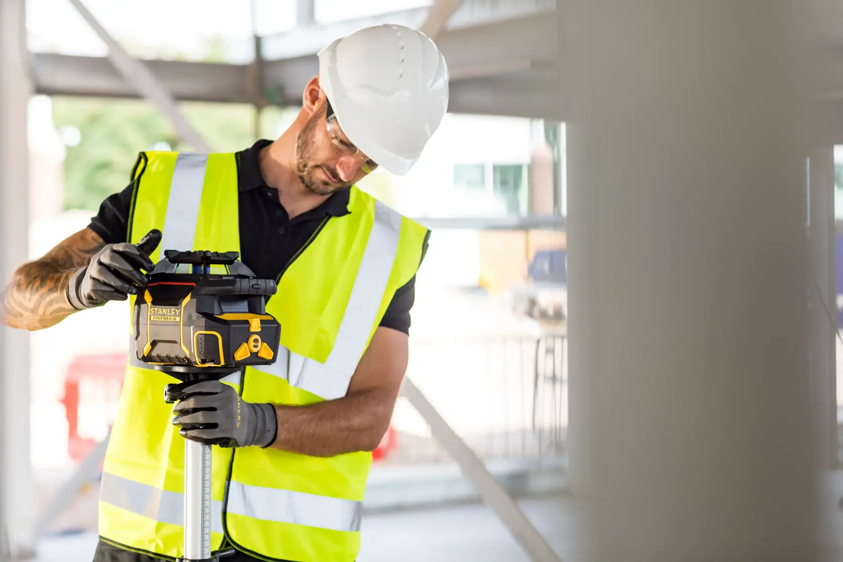 Photo of STANLEY FMHT77446-1 rotary laser level used by worker in high-visibility vest at construction site.