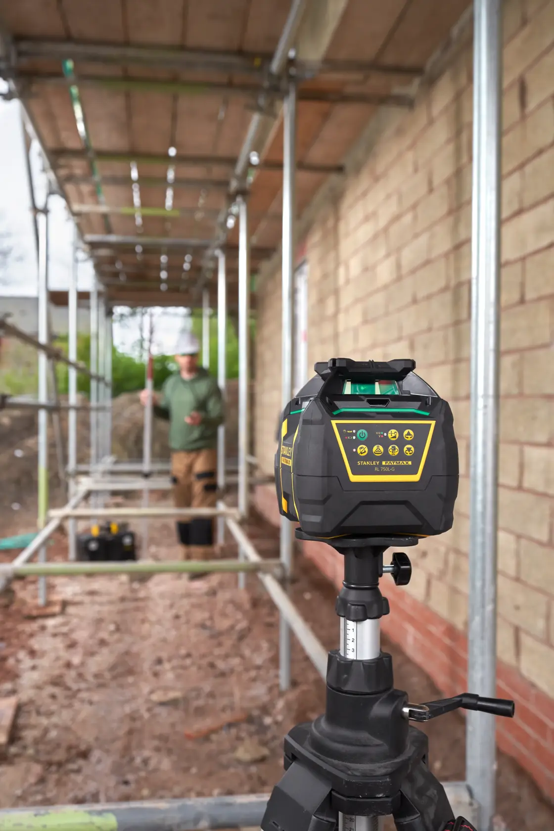 STANLEY FMHT77448 rotary laser level on tripod at construction site, focused on device with worker in background.