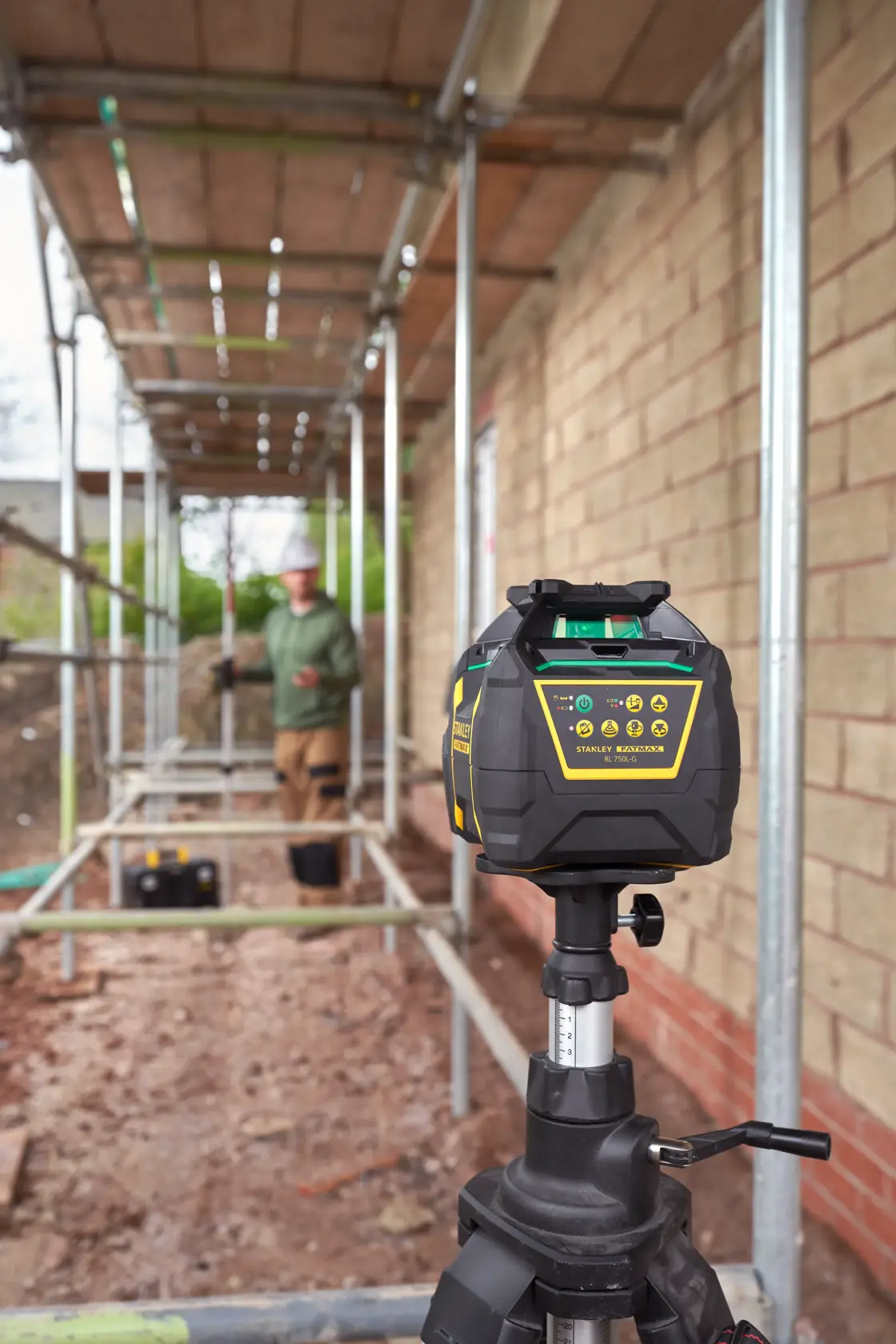 STANLEY FMHT77448 rotary laser level on tripod, construction site background, side angle.