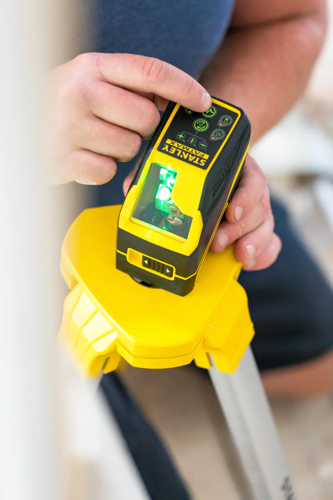 STANLEY FMHT77586-1 laser level on tripod, close-up of hand adjusting controls.