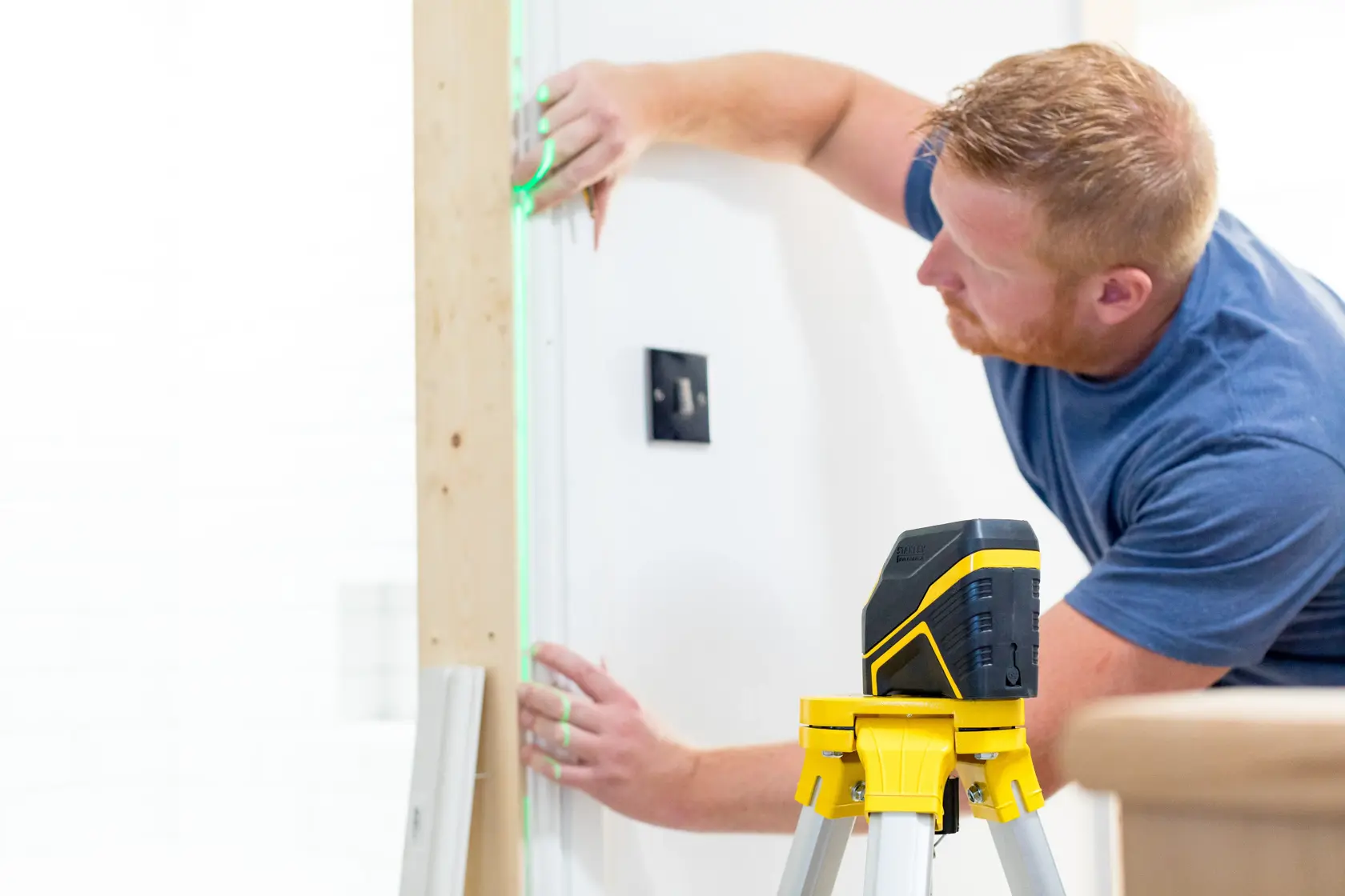 STANLEY FMHT77595-1 laser level on tripod, projecting green line onto wall during installation work.