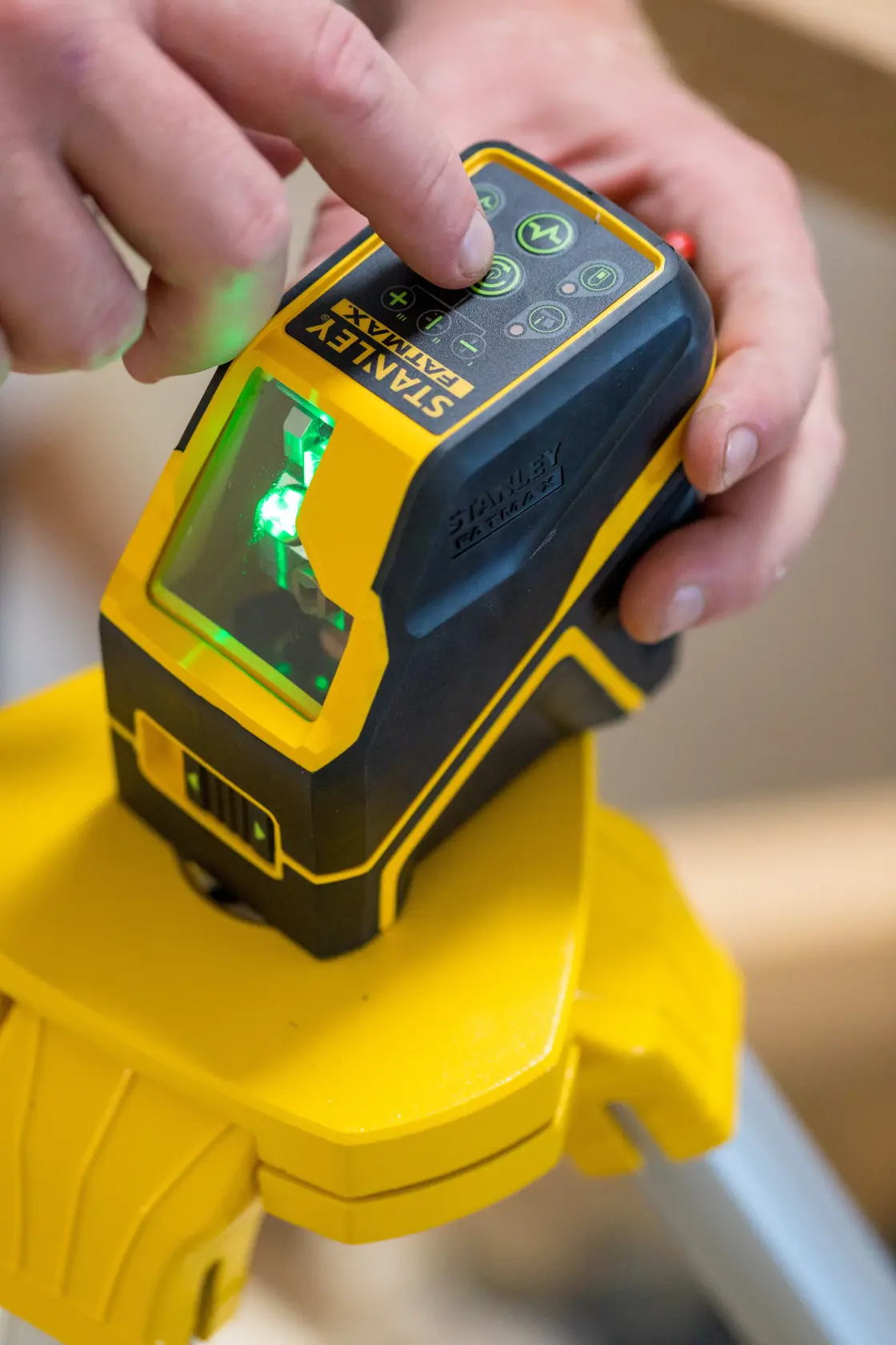 STANLEY FMHT77595-1 laser level on tripod, close-up of hand pressing control buttons with green laser on.