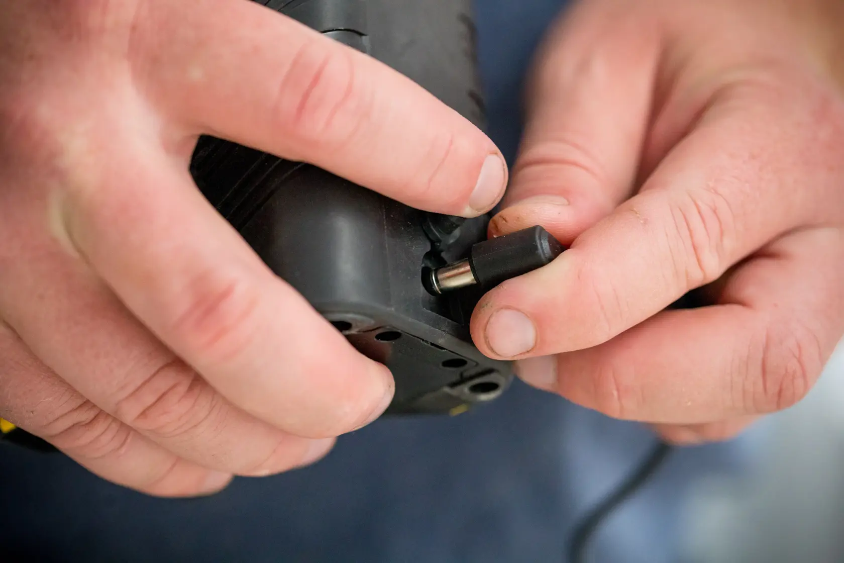 Photo of a hand connecting power adapter to STANLEY FMHT77598-1 device, close-up view, black casing.