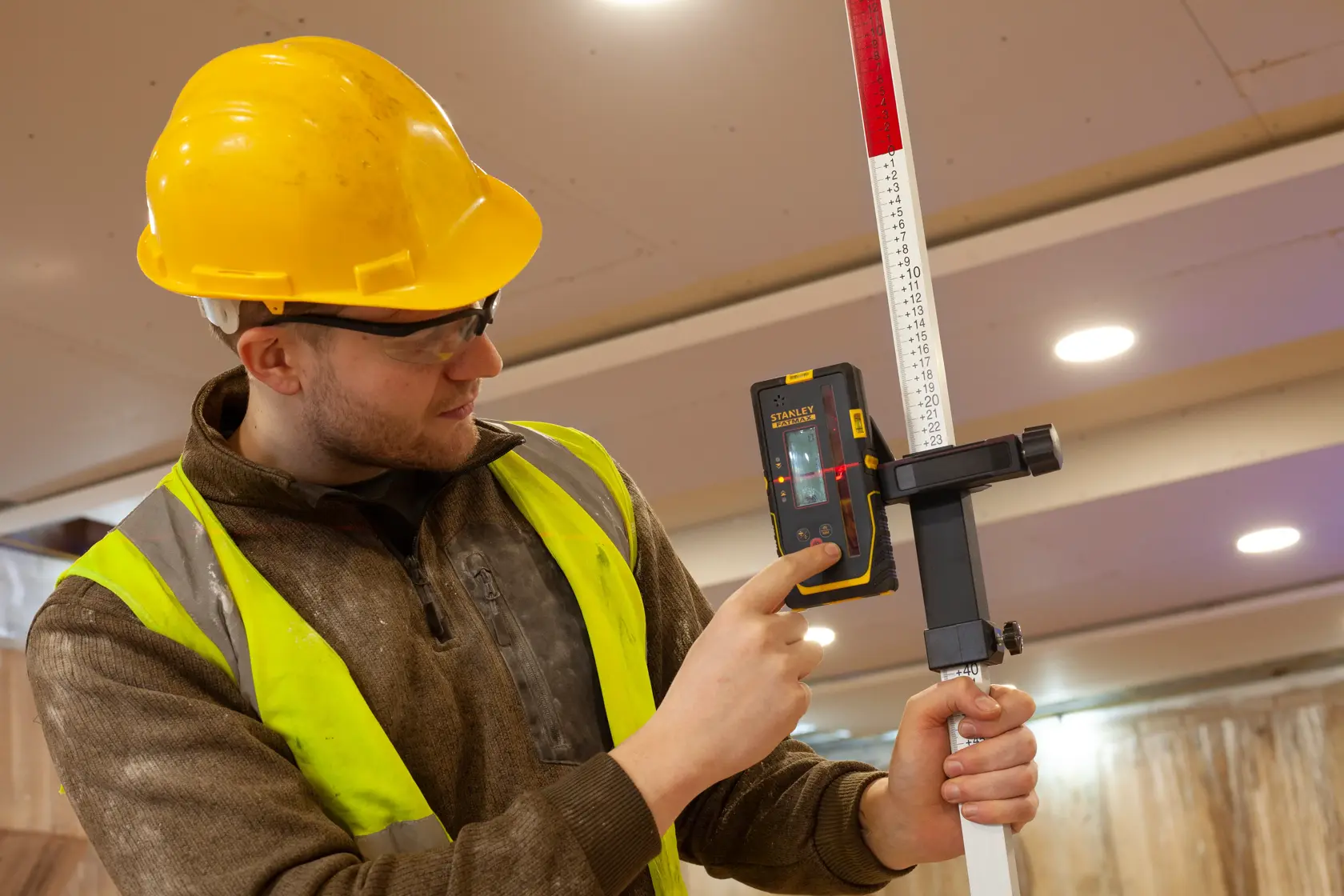 STANLEY FMHT77652-0 laser receiver held by worker on site, attached to measuring rod.