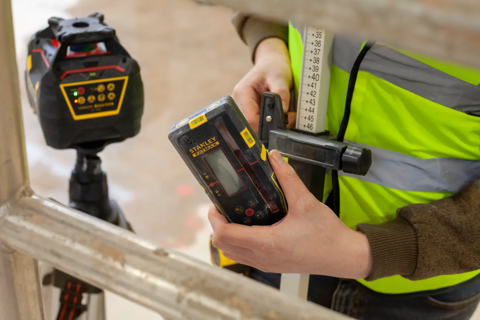 Photo of STANLEY FMHT77652-0 laser detector held in hand, with laser level device in background, construction setting.
