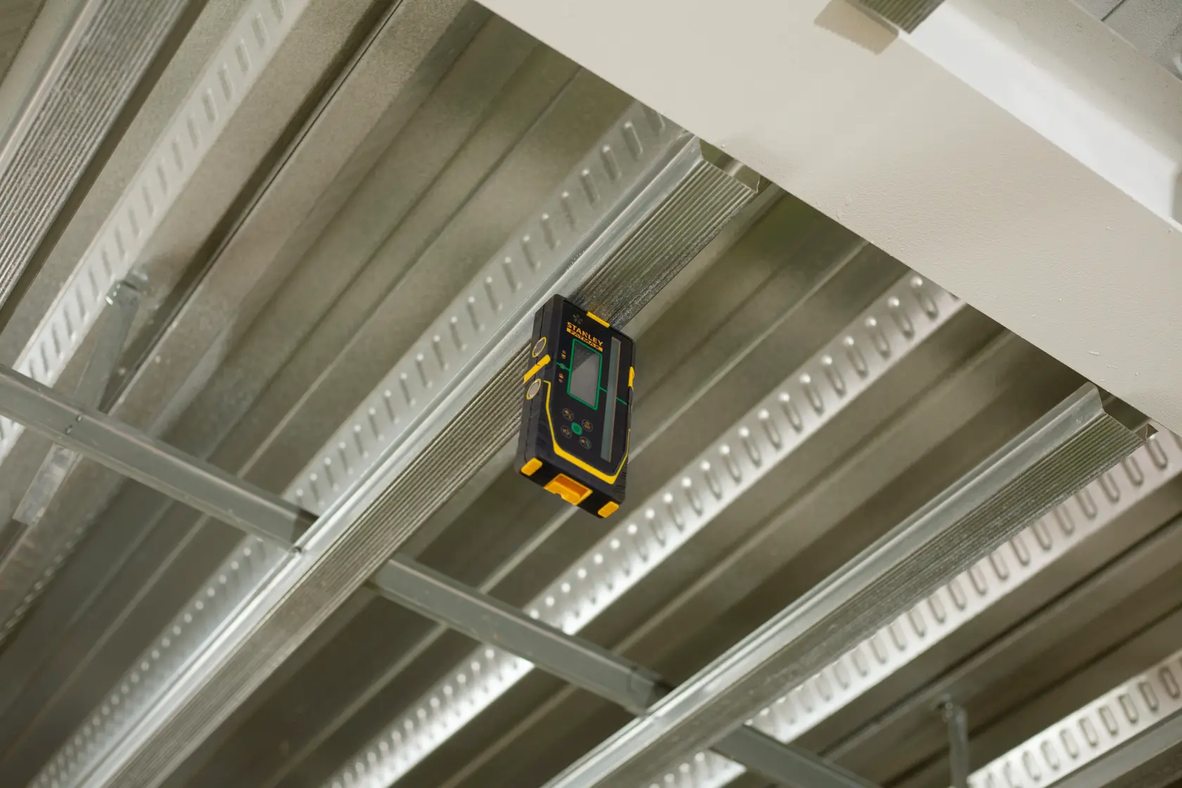 Photo of STANLEY FMHT77653-0 laser detector attached to a metal ceiling frame, showing front display.