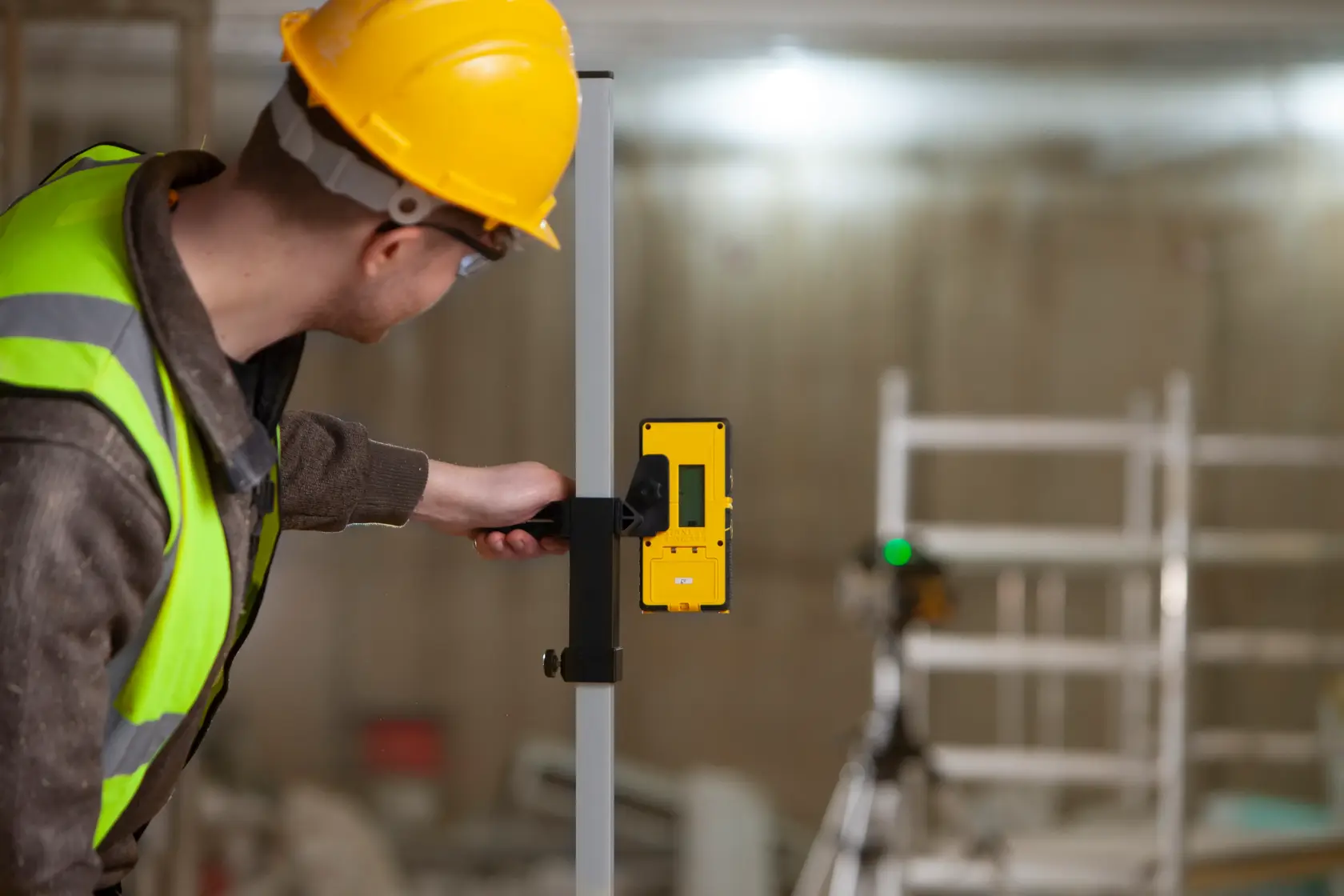 Photo of a worker using a STANLEY FMHT77653-0 laser detector attached to a rod at a construction site.