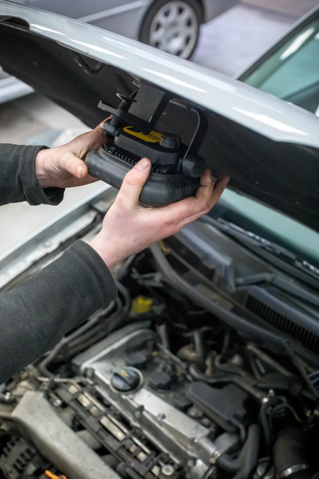 Photo of a person attaching a STANLEY FMHT81507-1 work light under a car hood, focusing on the installation process.