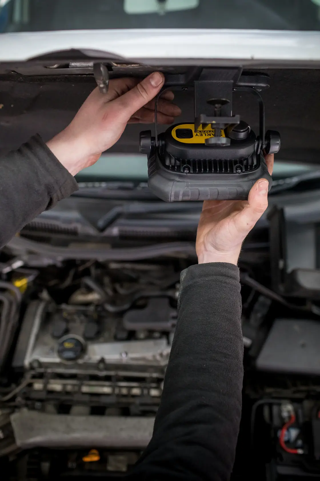 STANLEY FMHT81507-1 work light mounted under car hood, hands adjusting light, automotive repair context.