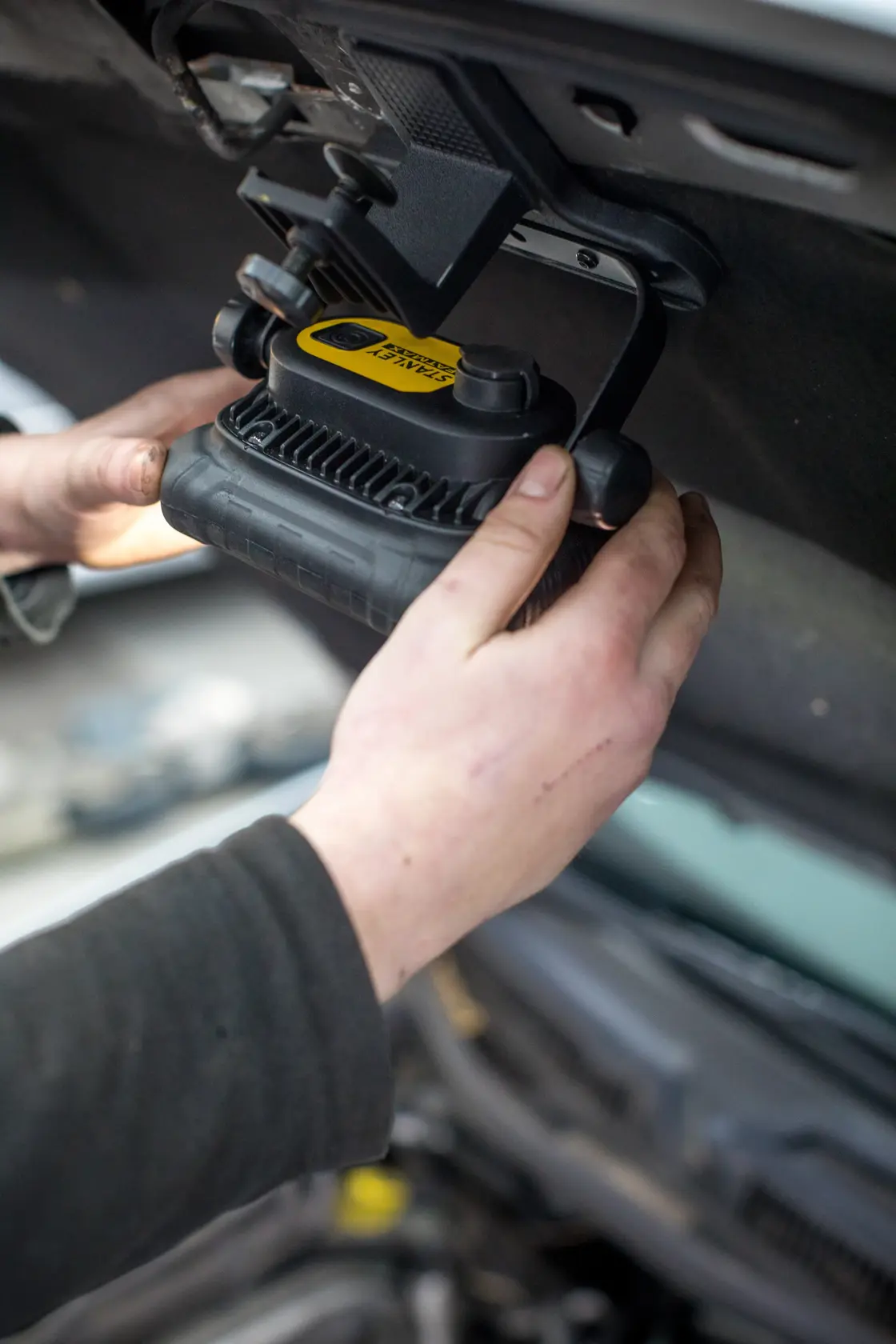 STANLEY FMHT81507-1 work light mounted under car hood in use, hands adjusting black and yellow light.