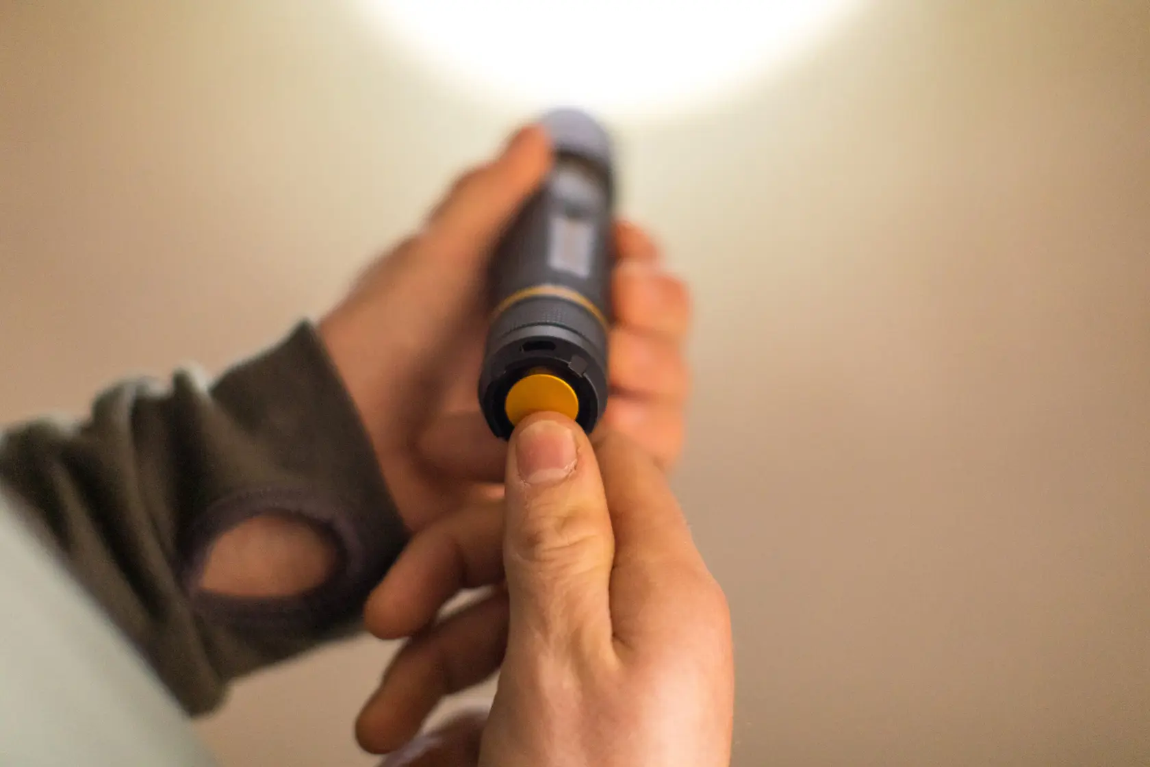 STANLEY FMHT81511-0 flashlight in hand, showing yellow button being pressed, close-up photography.