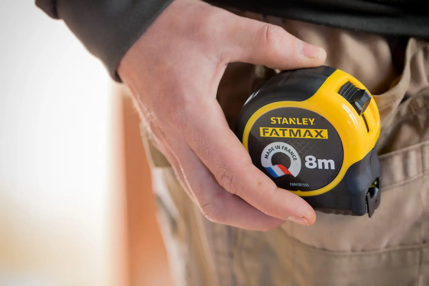 Photo of STANLEY FMHT81555-0 FATMAX 8m tape measure held in a hand, clipped to beige work trousers.