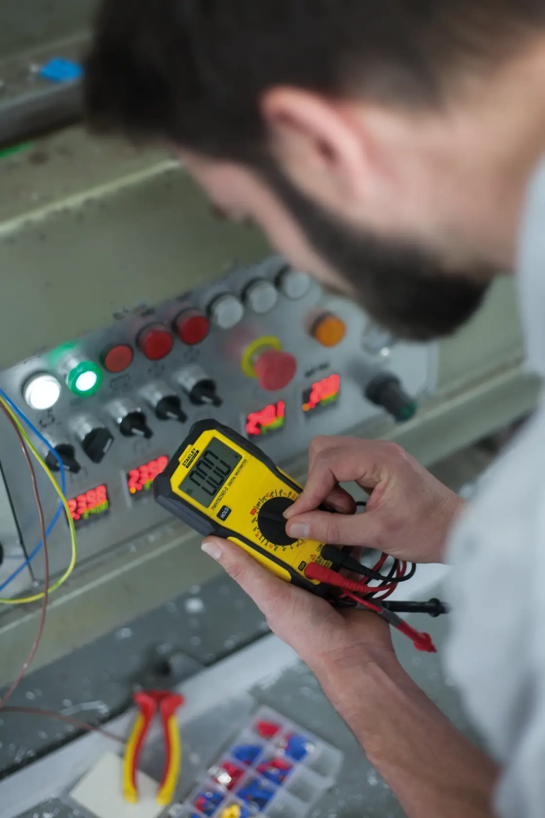Photo of STANLEY FMHT82565-0 digital multimeter being used to measure a control panel; yellow and black device.