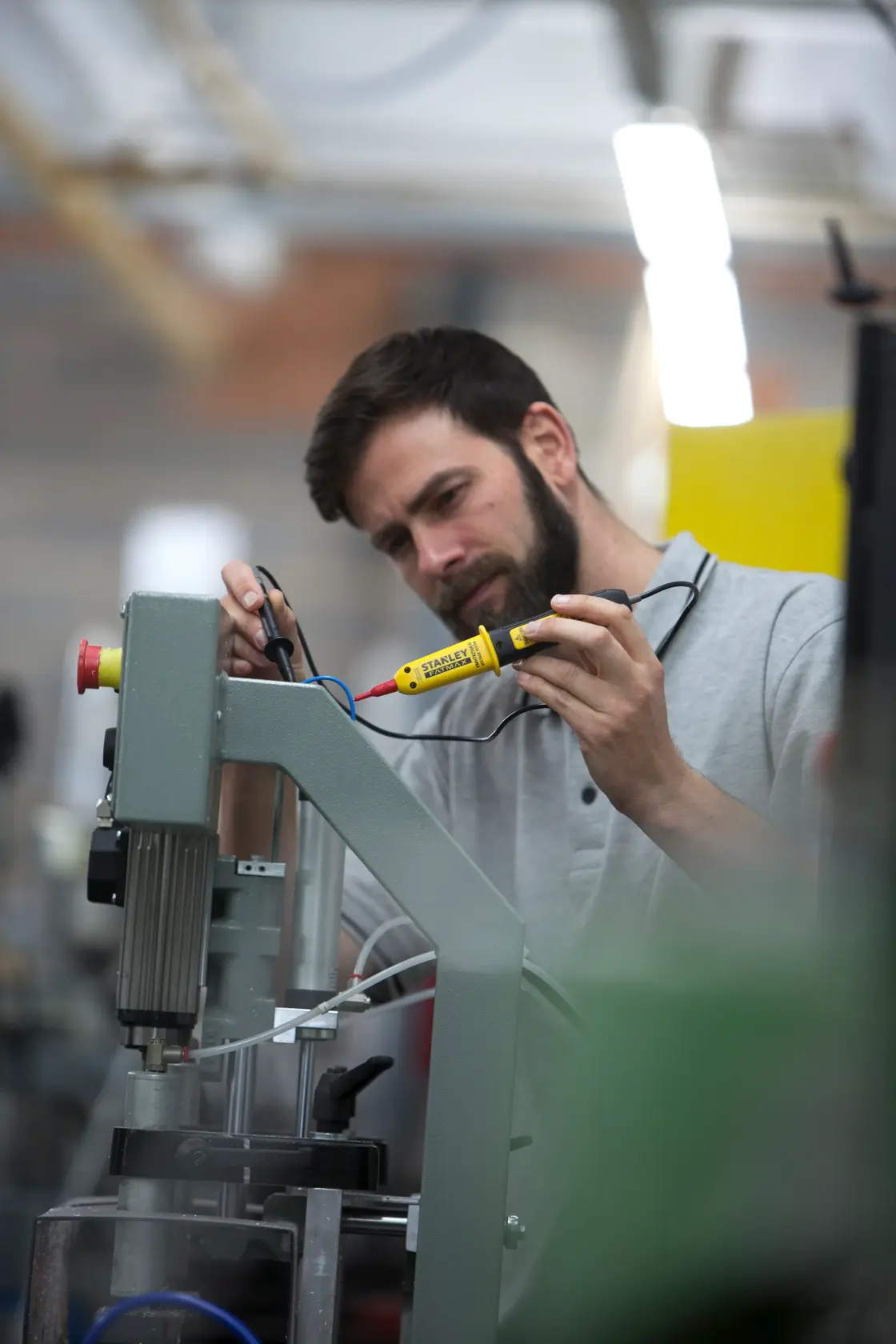 Photo of STANLEY FMHT82566-0 voltage tester in use, worker checking machine wiring in industrial setting.