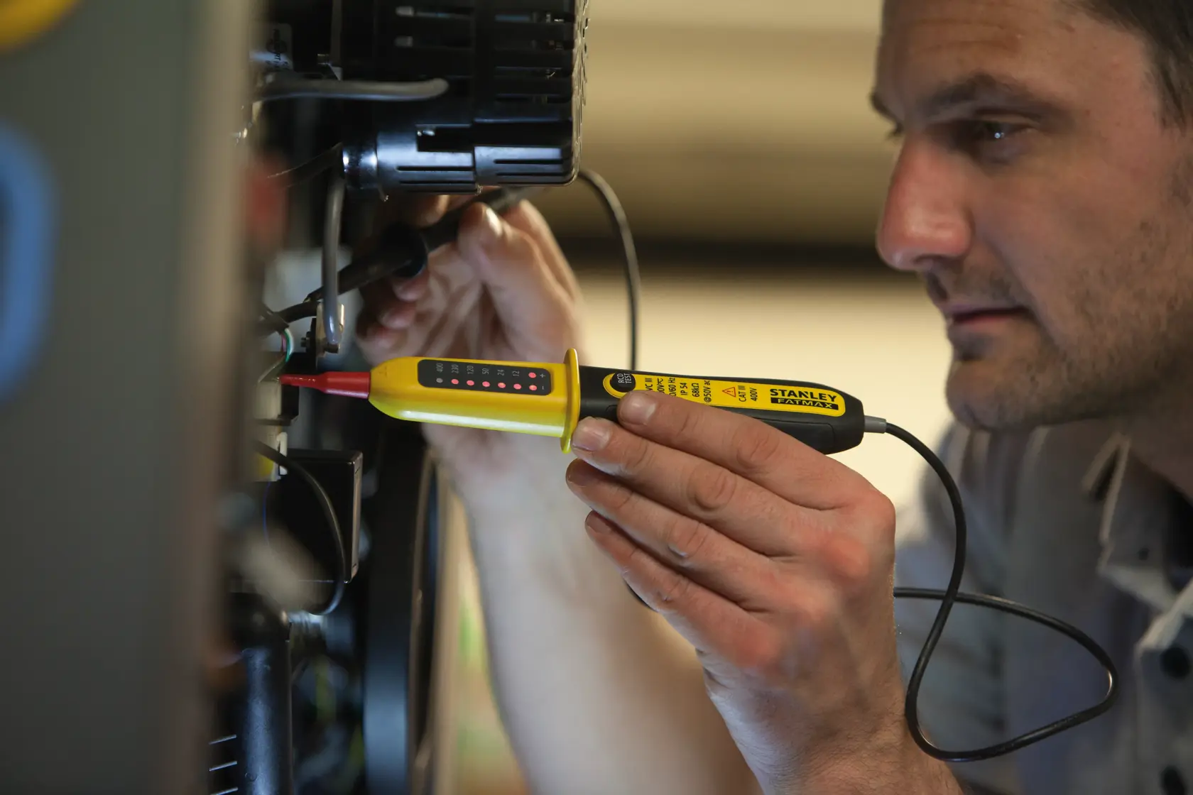 STANLEY FMHT82566-0 voltage tester in use, yellow handheld tool with LED indicators, close-up in electrical setting.