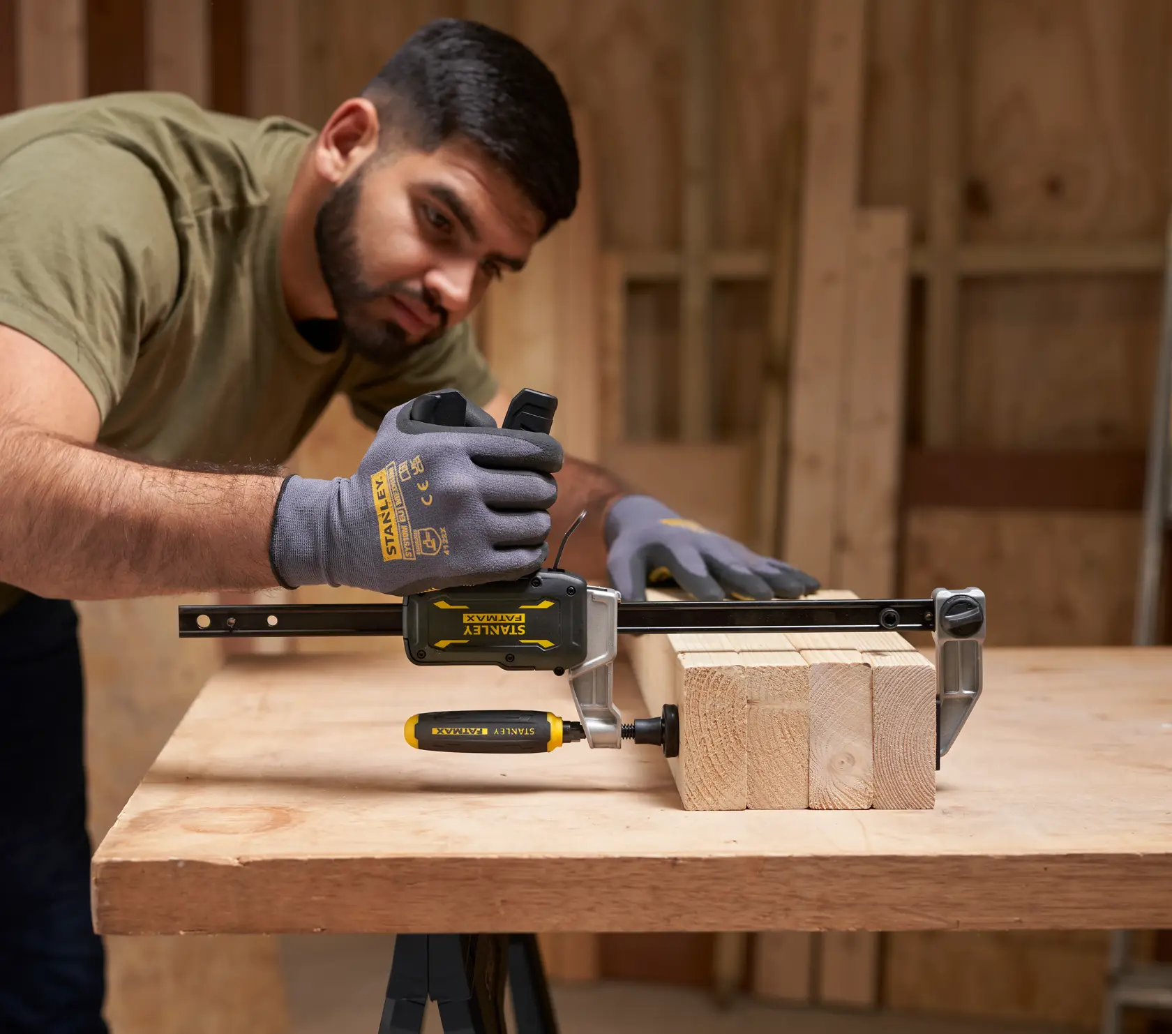 STANLEY FMHT83006-0 clamp in use on wooden boards, gloved hands adjusting clamp, woodworking setting.
