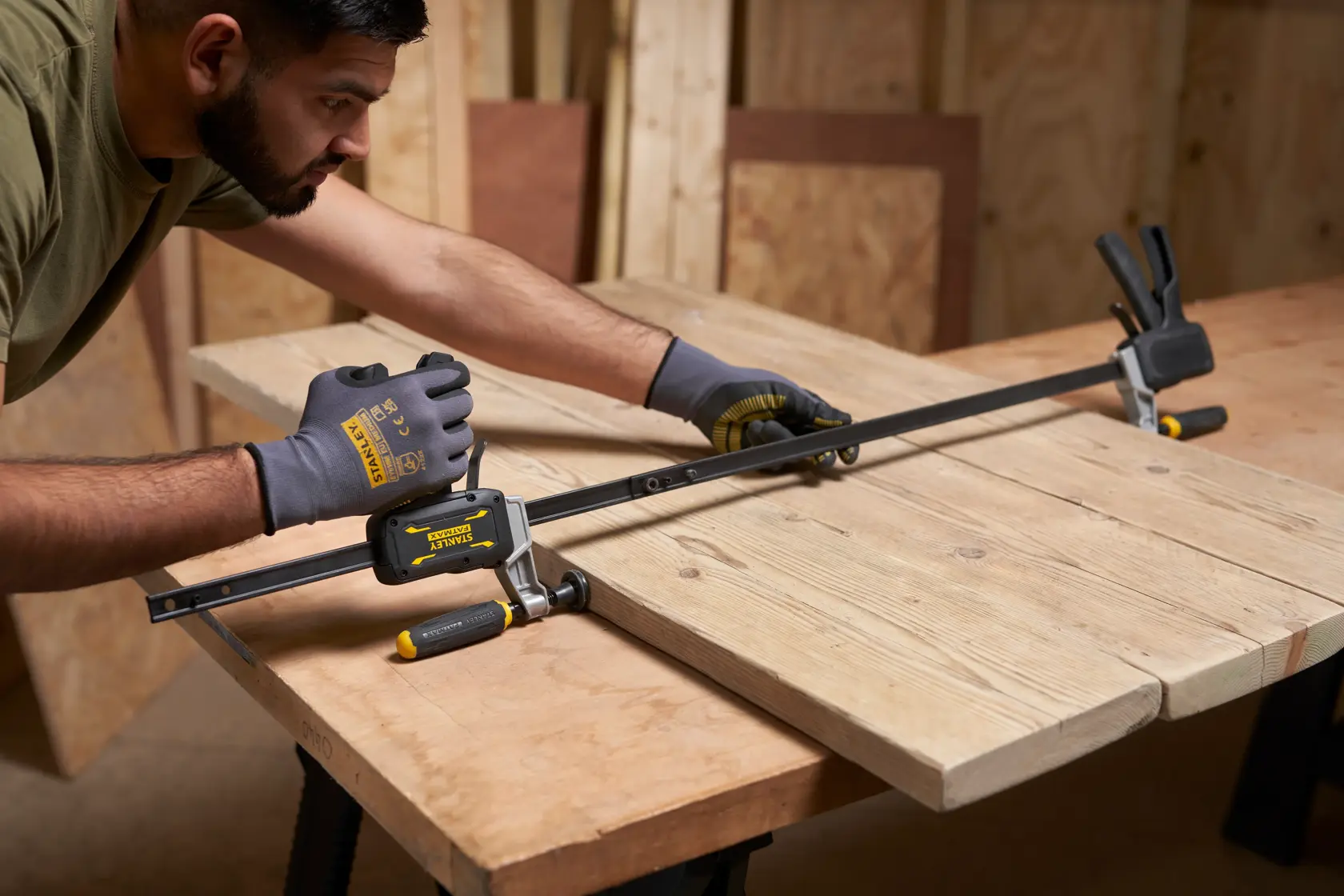 Stanley FMHT83007-0 clamp in use, holding wooden boards on workbench in woodworking workshop.