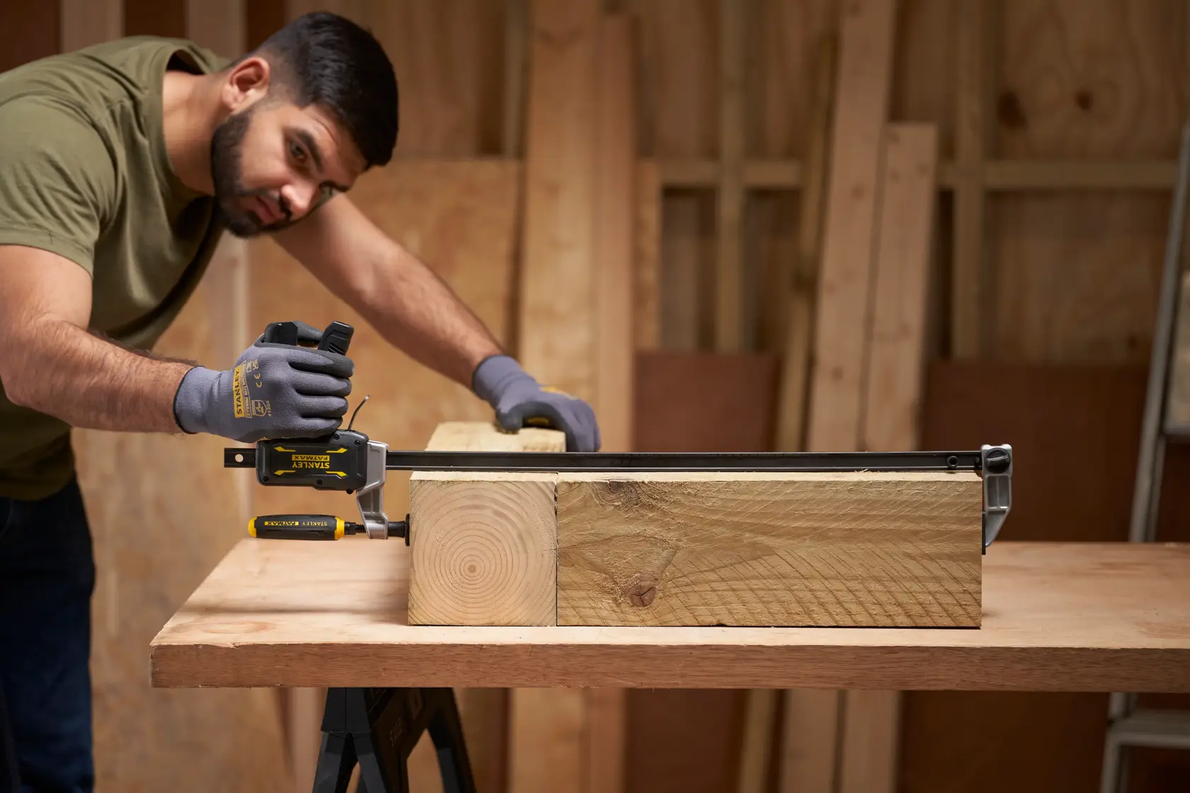 STANLEY FMHT83008-0 clamp holding thick wooden beam on workbench in a workshop setting.
