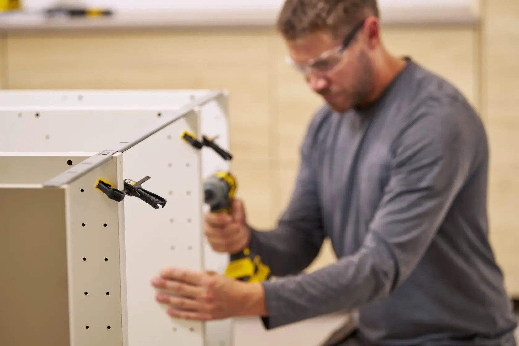 STANLEY FMHT83270-0 clamp securing white cabinet panels during assembly, person using power drill.