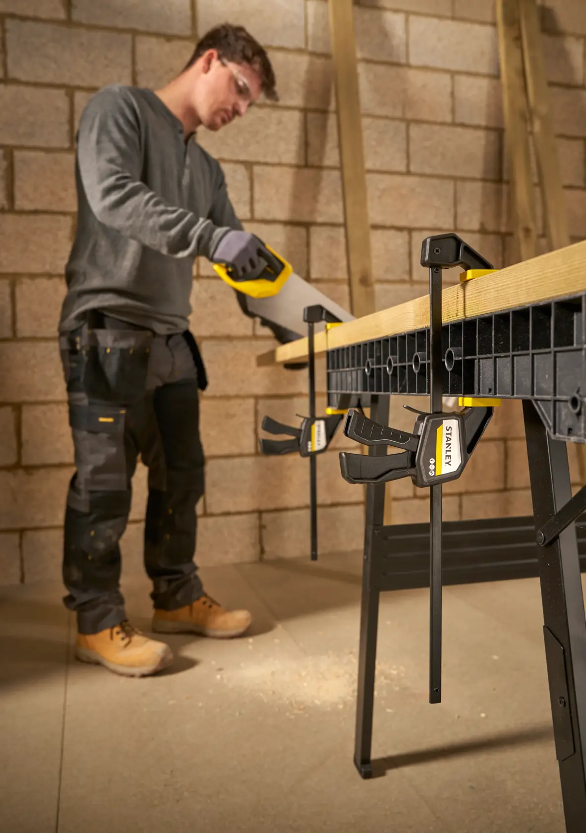STANLEY FMHT83272-0 bar clamps securing wood on workbench, side angle, carpenter sawing in workshop.
