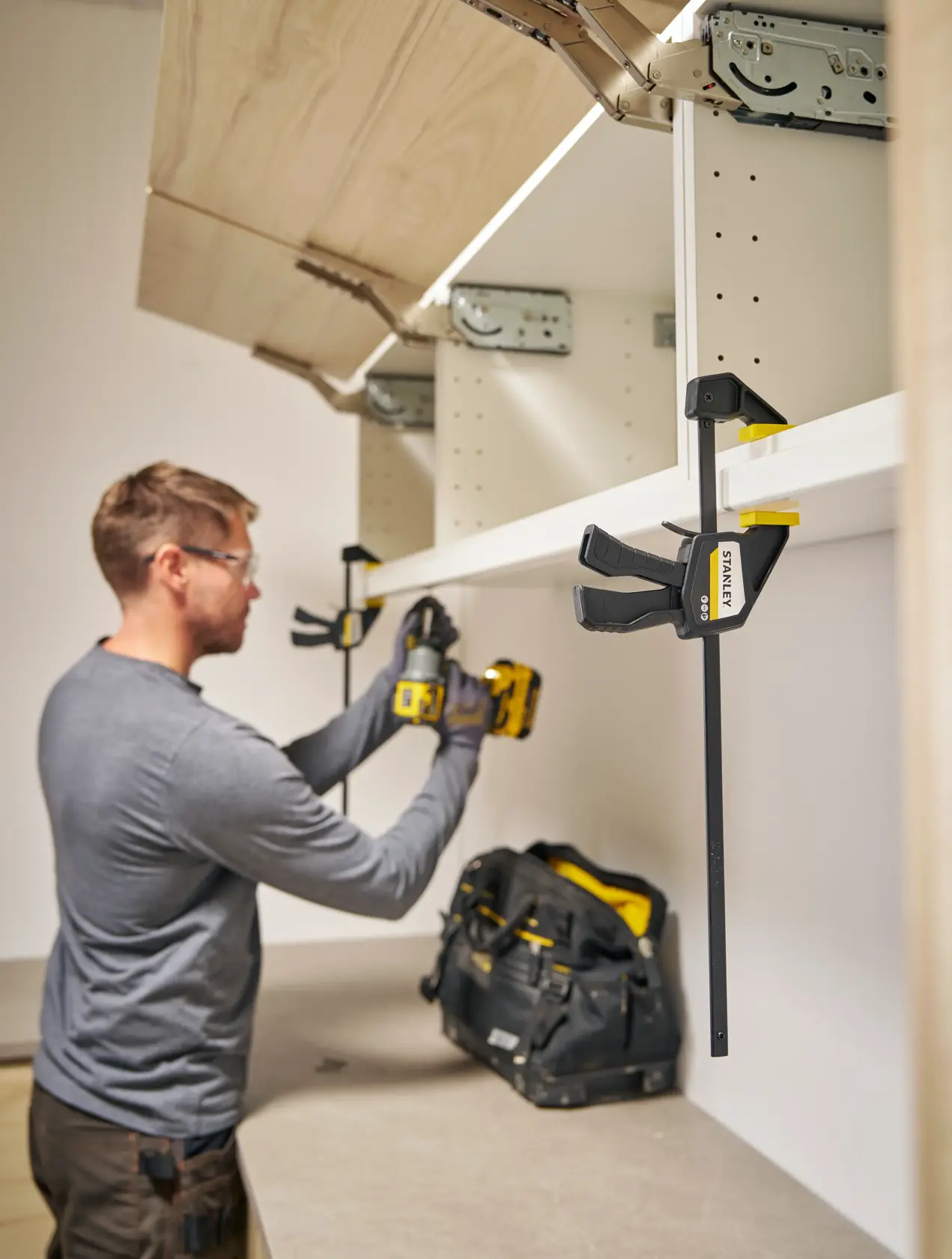 STANLEY FMHT83272-0 quick-adjust bar clamp holding shelf during installation, workshop setting.