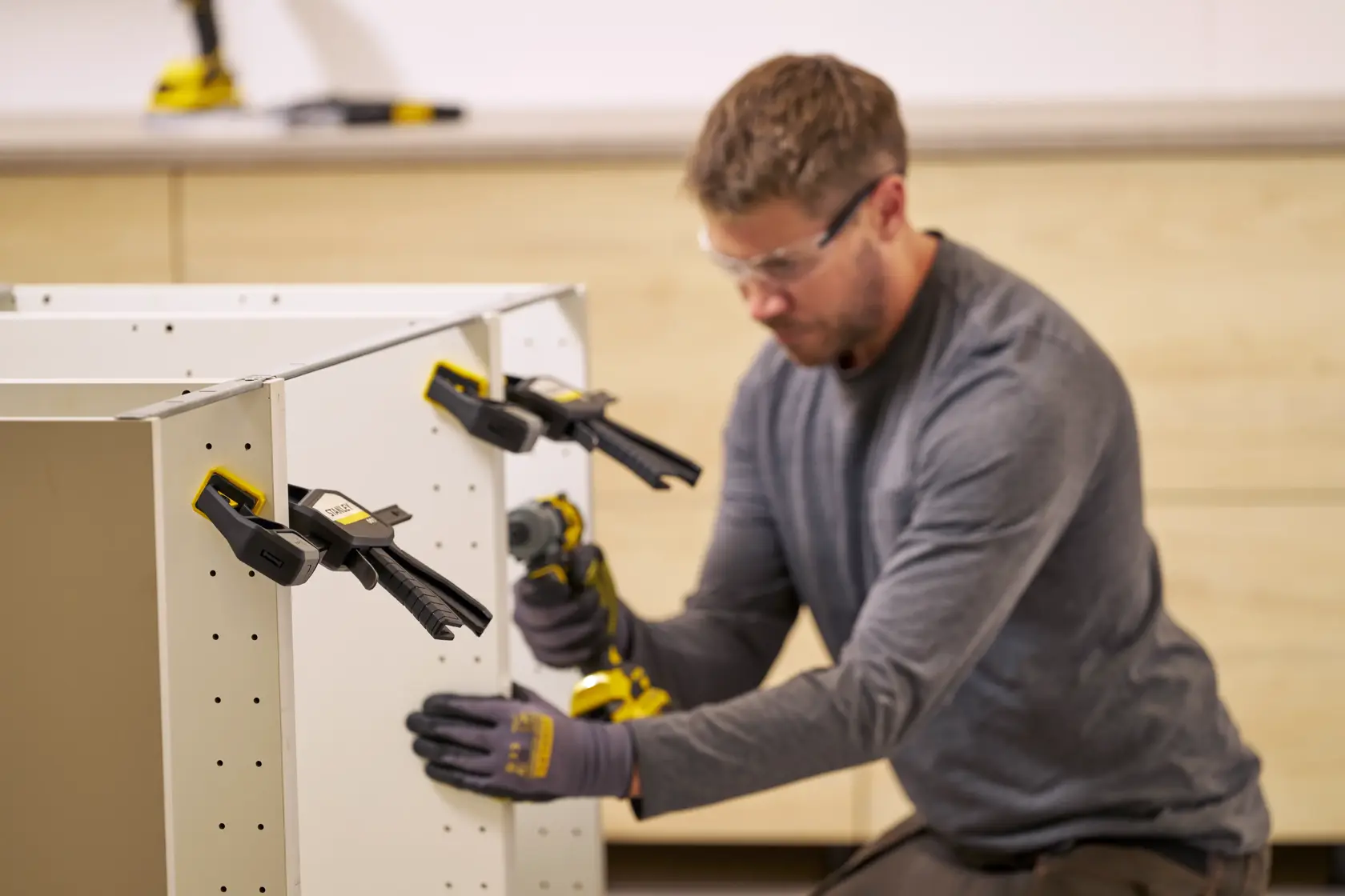 STANLEY FMHT83273-0 clamps securing white cabinet panels during assembly, close-up, workshop setting.