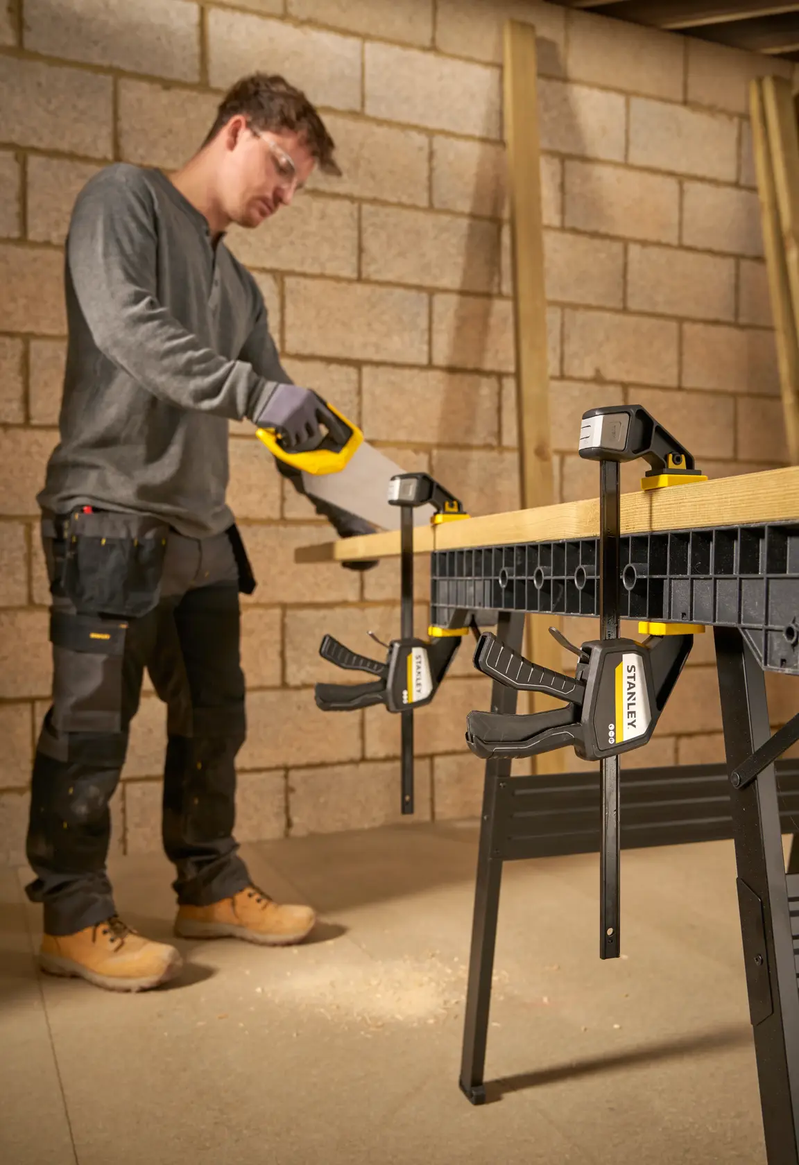 Photo of STANLEY FMHT83274-0 clamp securing wood on workbench during sawing, product in workshop setting.