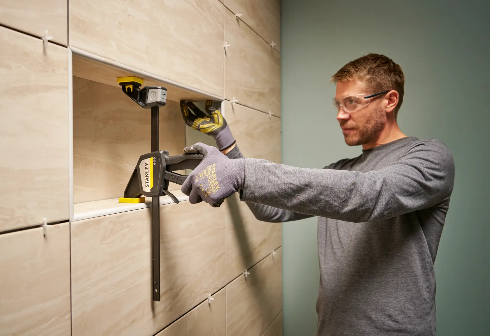 Photo of STANLEY FMHT83274-0 large bar clamp in use holding tiles on wall during installation.
