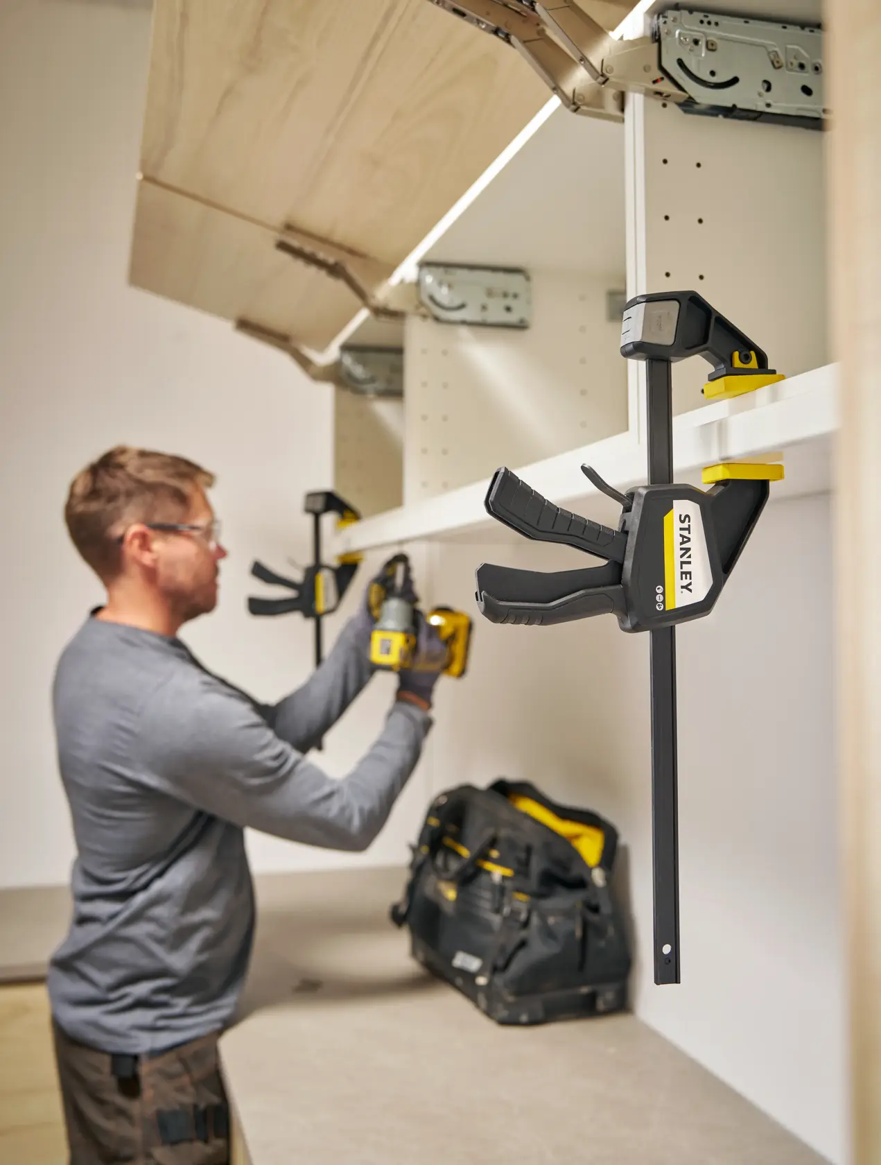 Photo of STANLEY FMHT83274-0 bar clamp in use during cabinet installation, tool bag visible on counter.