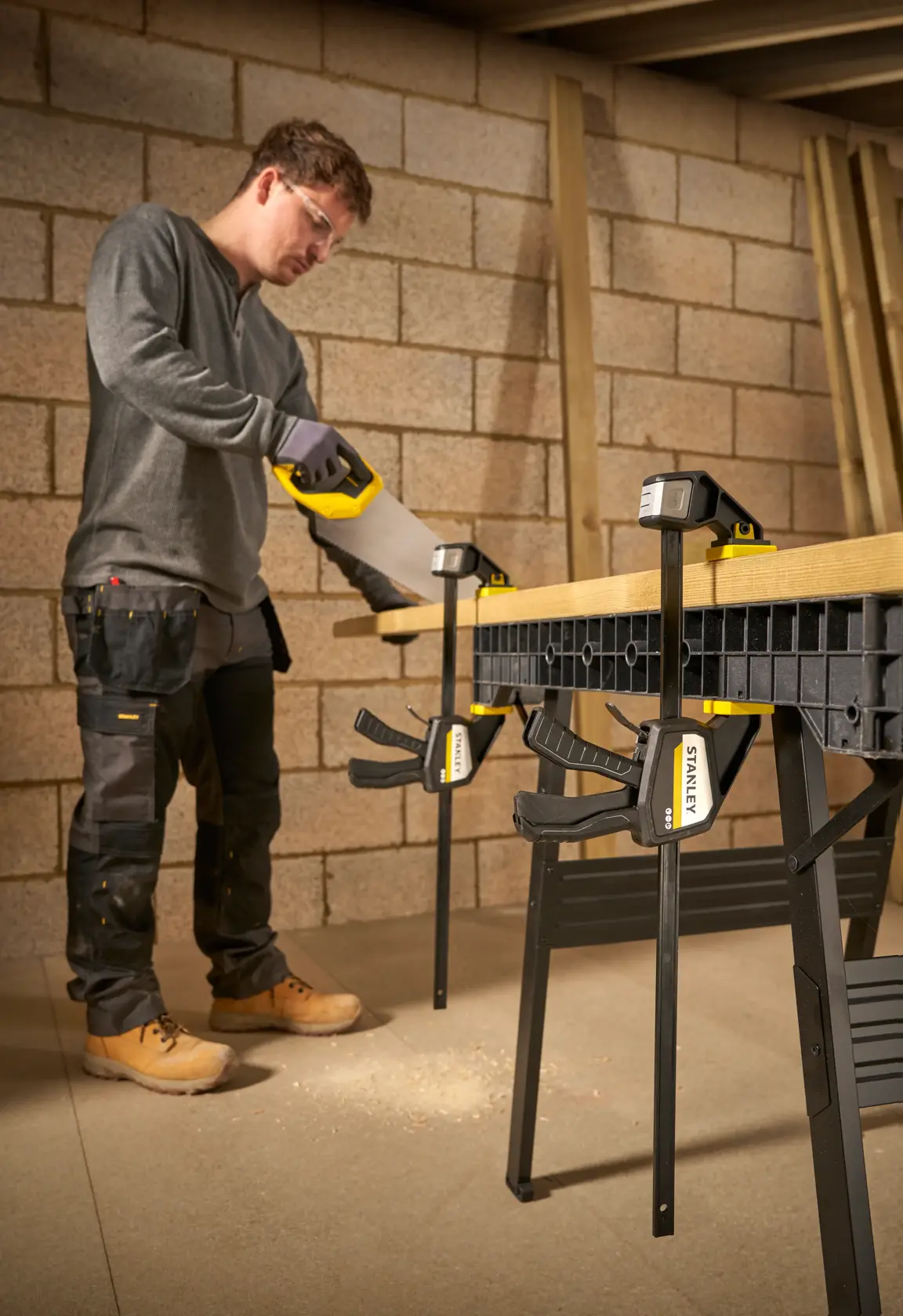 Photo of STANLEY FMHT83275-0 bar clamps securing wood to a workbench during sawing in a workshop.