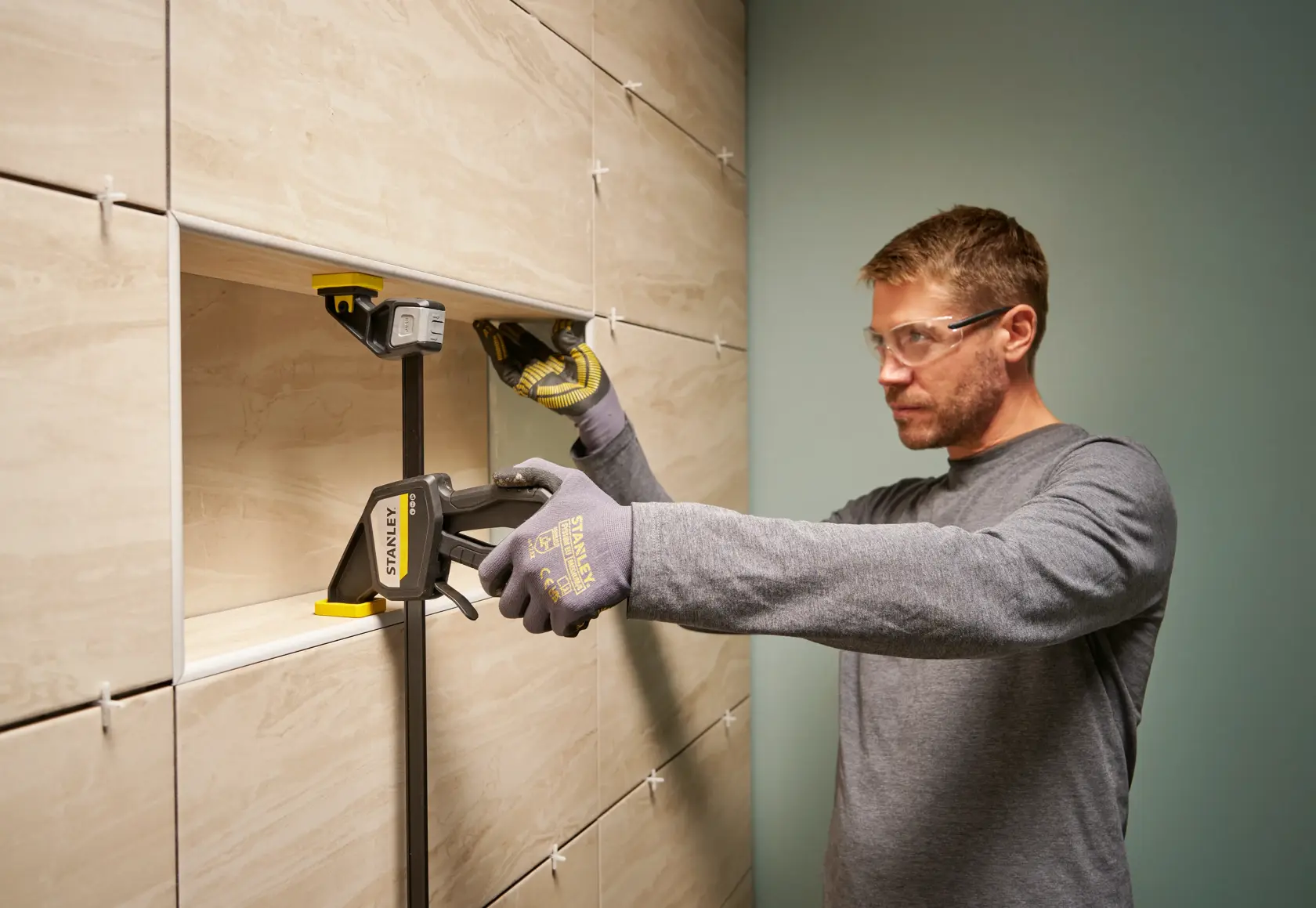 Photo of a worker using a STANLEY FMHT83275-0 clamp to secure tiles during installation on a wall.
