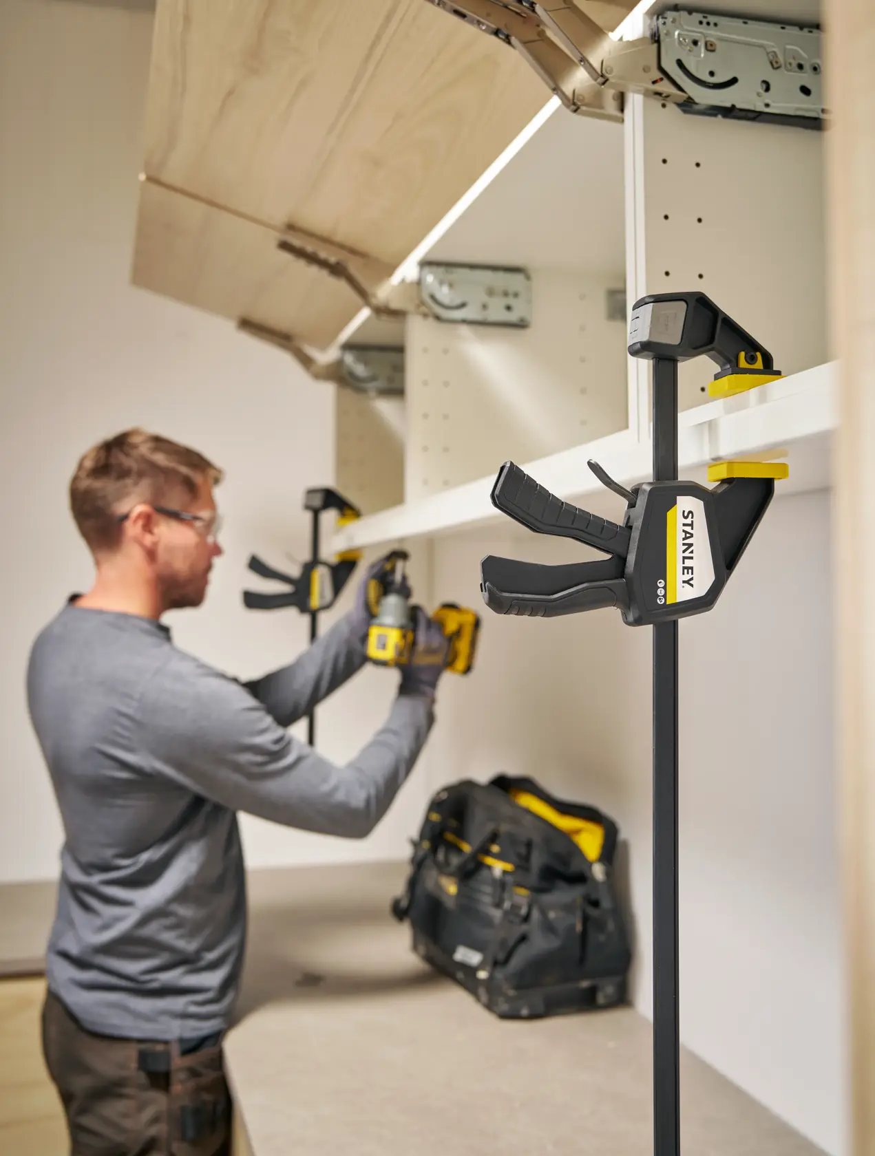Photo of STANLEY FMHT83275-0 bar clamp holding a white shelf during installation in a workshop.