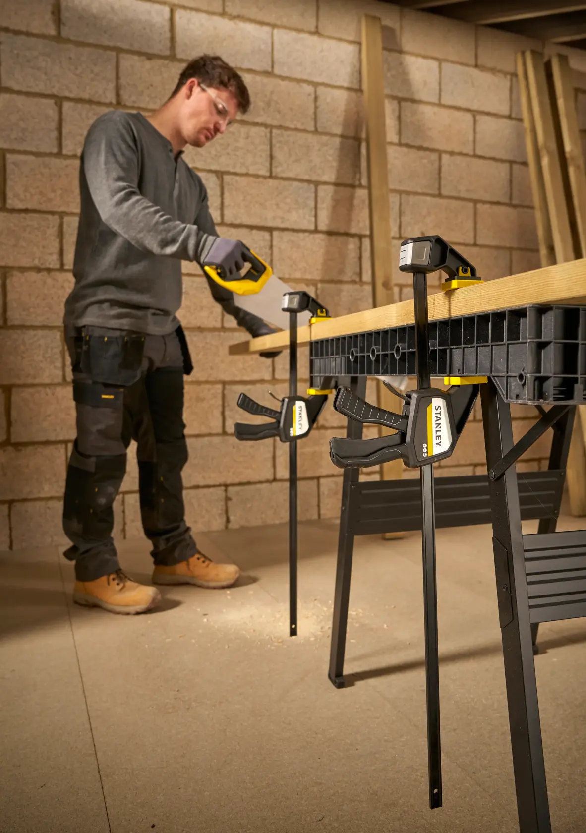 Photo of STANLEY FMHT83276-0 bar clamps securing wood on workbench, used by worker in workshop.