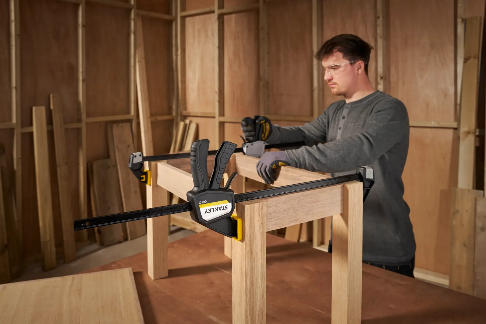 STANLEY FMHT83276-0 bar clamp securing wood frame in workshop, person assembling furniture.