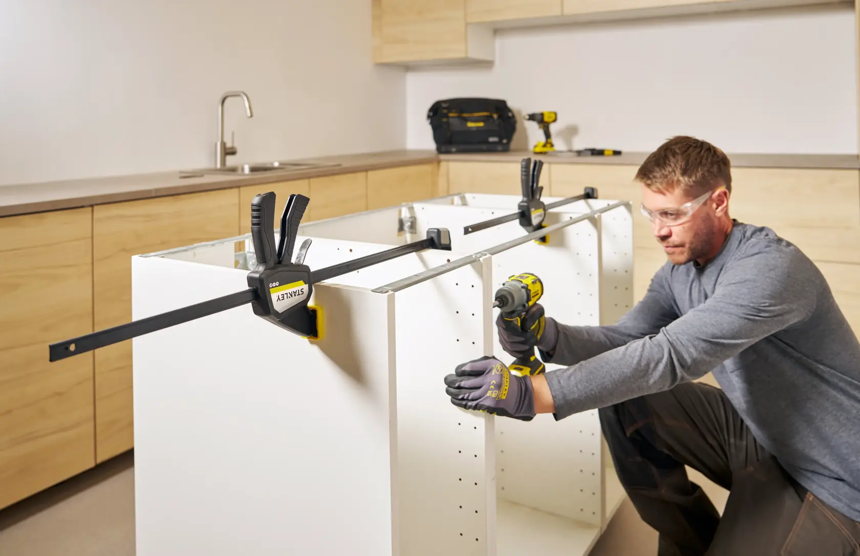 Photo of STANLEY FMHT83276-0 bar clamp securing white cabinet panels during assembly in a modern kitchen.