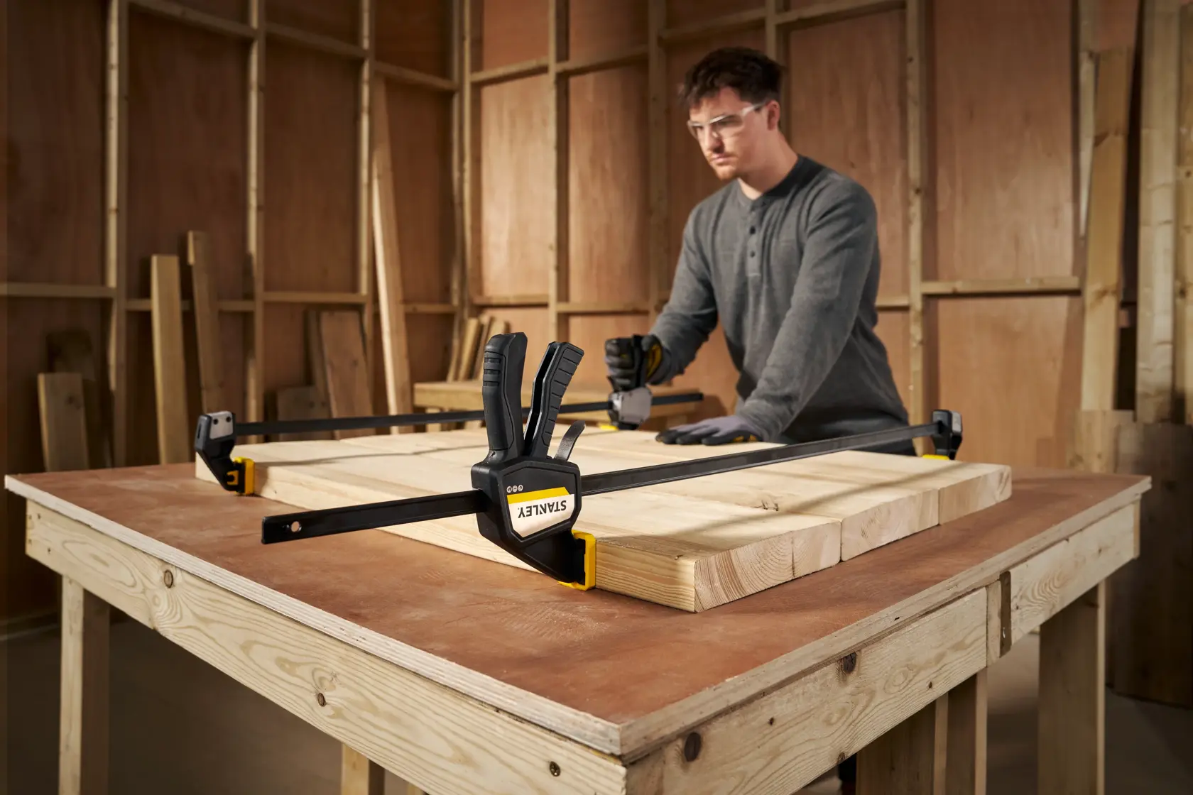 STANLEY FMHT83277-0 bar clamp securing wood pieces on a workbench in a workshop setting.