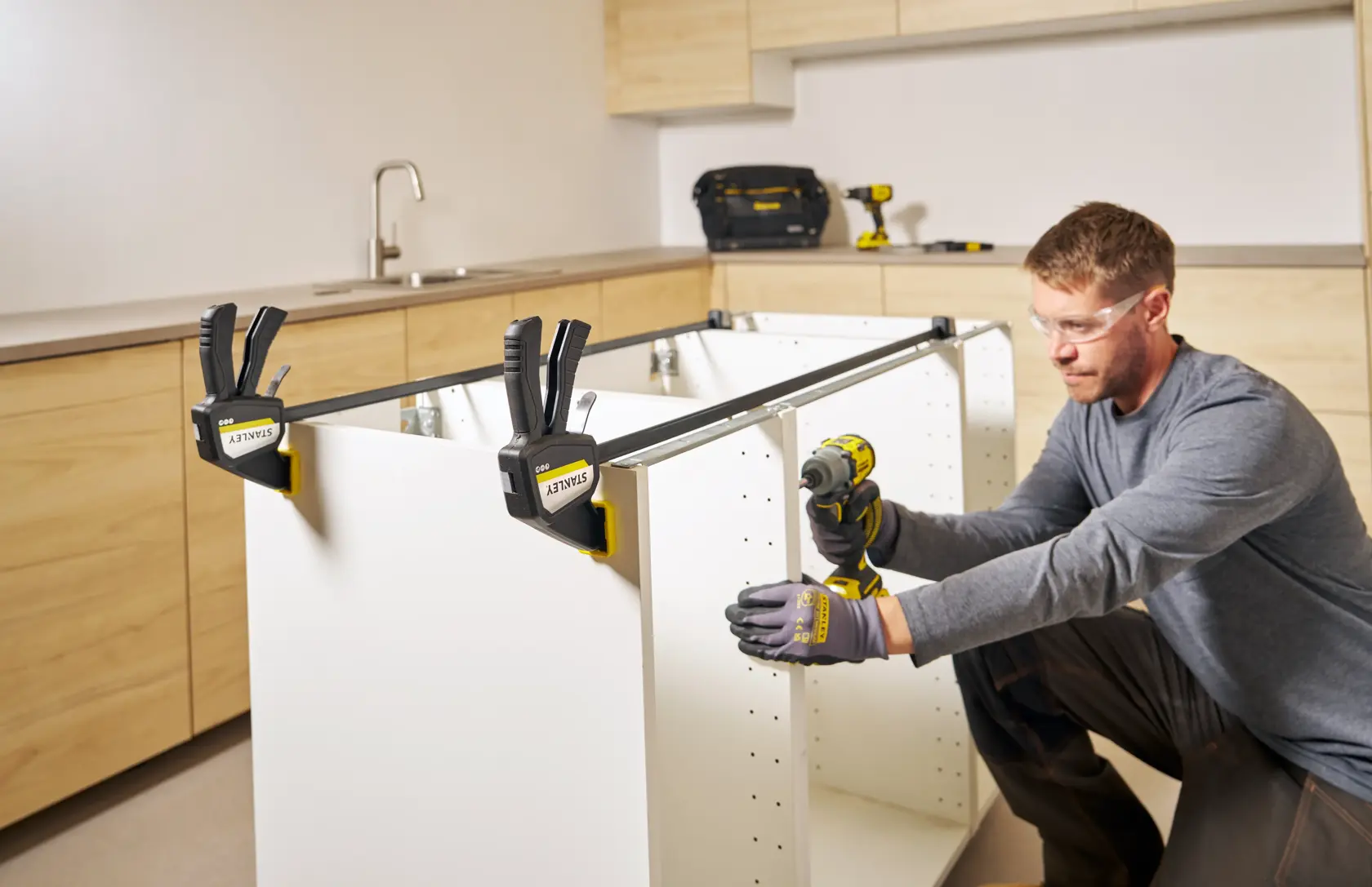 Photo of STANLEY FMHT83277-0 bar clamps securing a cabinet frame during assembly in a workshop setting.