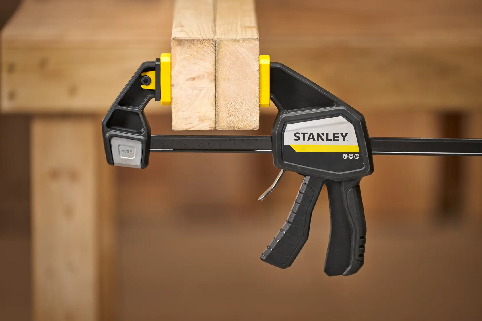 STANLEY FMHT83277-0 trigger clamp holding two wooden boards on a workbench, side view.