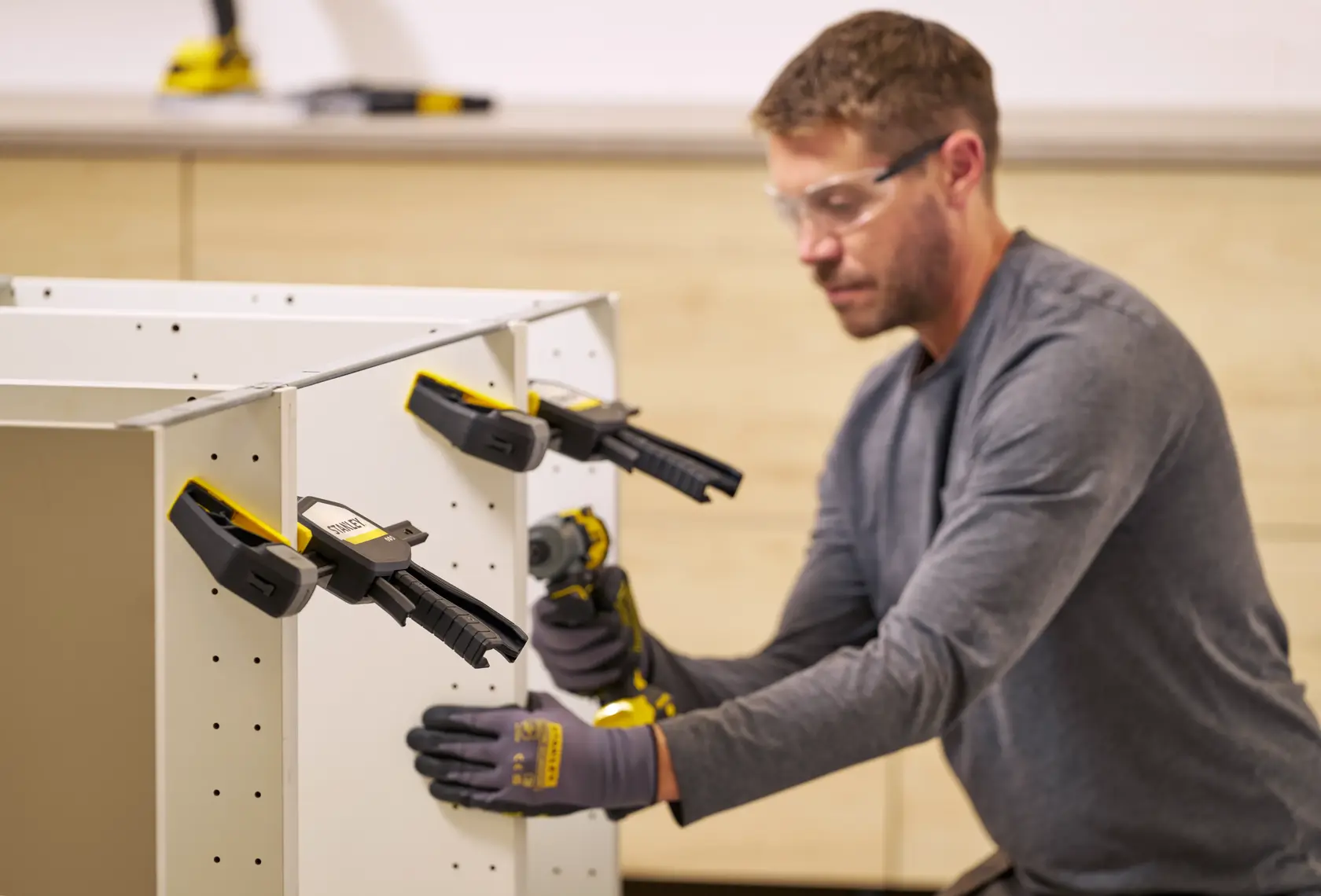 STANLEY FMHT83278-0 bar clamps holding white furniture panels, person assembling cabinet in workshop.