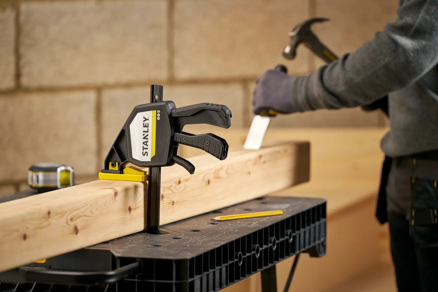 STANLEY FMHT83278-0 clamp secures wood on workbench, close-up photo in workshop with carpenter.