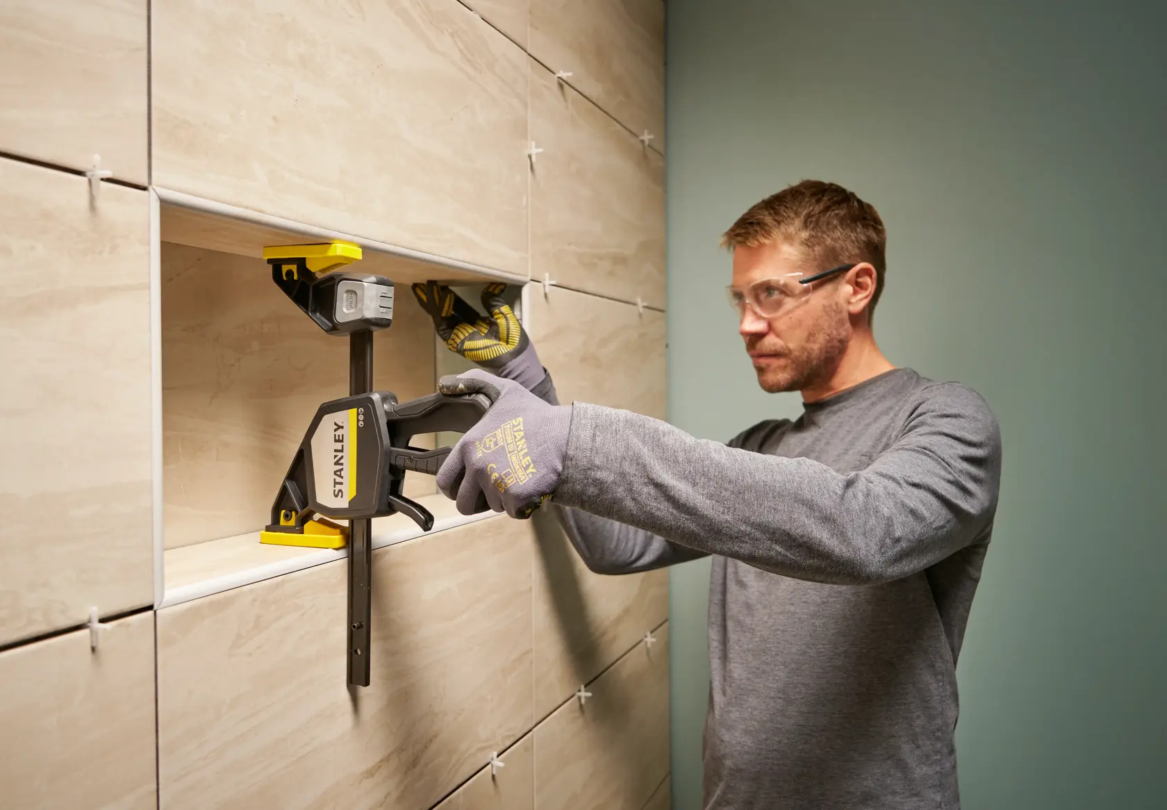 STANLEY FMHT83278-0 clamp used for tile installation on a wall, person wearing gloves.