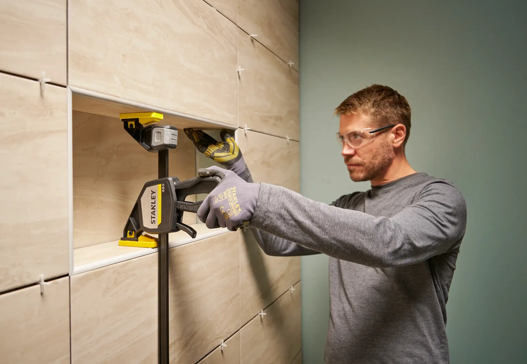 Photo of STANLEY FMHT83280-0 clamp used to secure tiles during installation, person wearing gloves adjusting tiles.