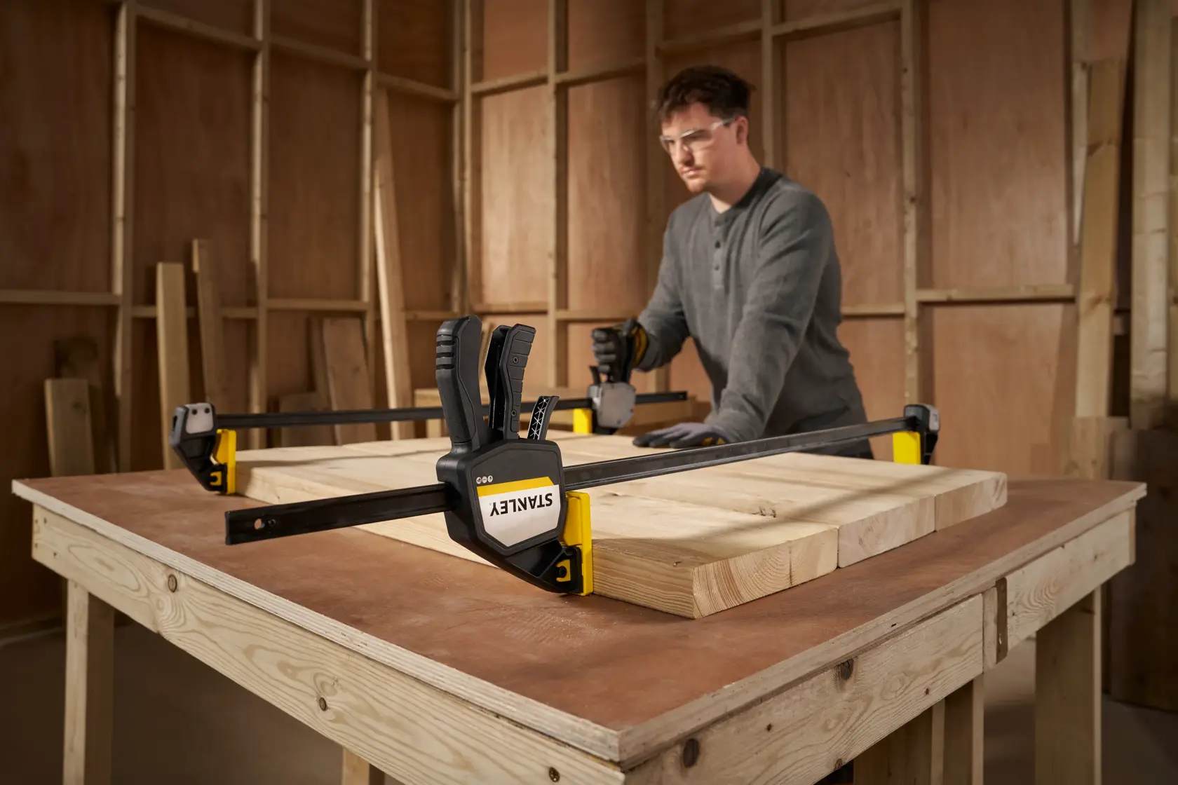 STANLEY FMHT83282-0 bar clamp holding wood boards on a workbench, workshop background.