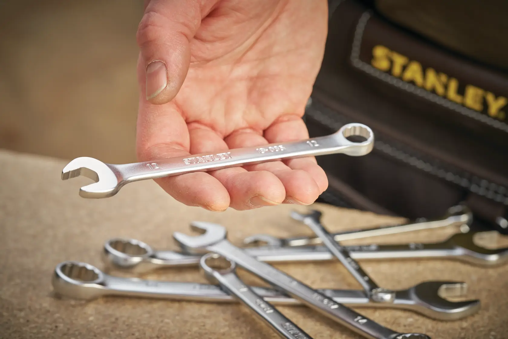 Stanley FMMT13029-0 combination wrench held in hand with other wrenches on table, photography close-up.