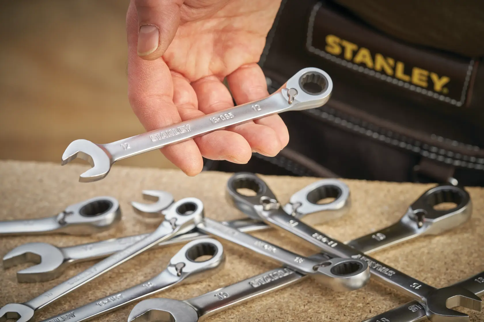 Stanley FMMT13094-0 ratcheting spanner held in hand, with other wrenches on work surface, close-up angle.