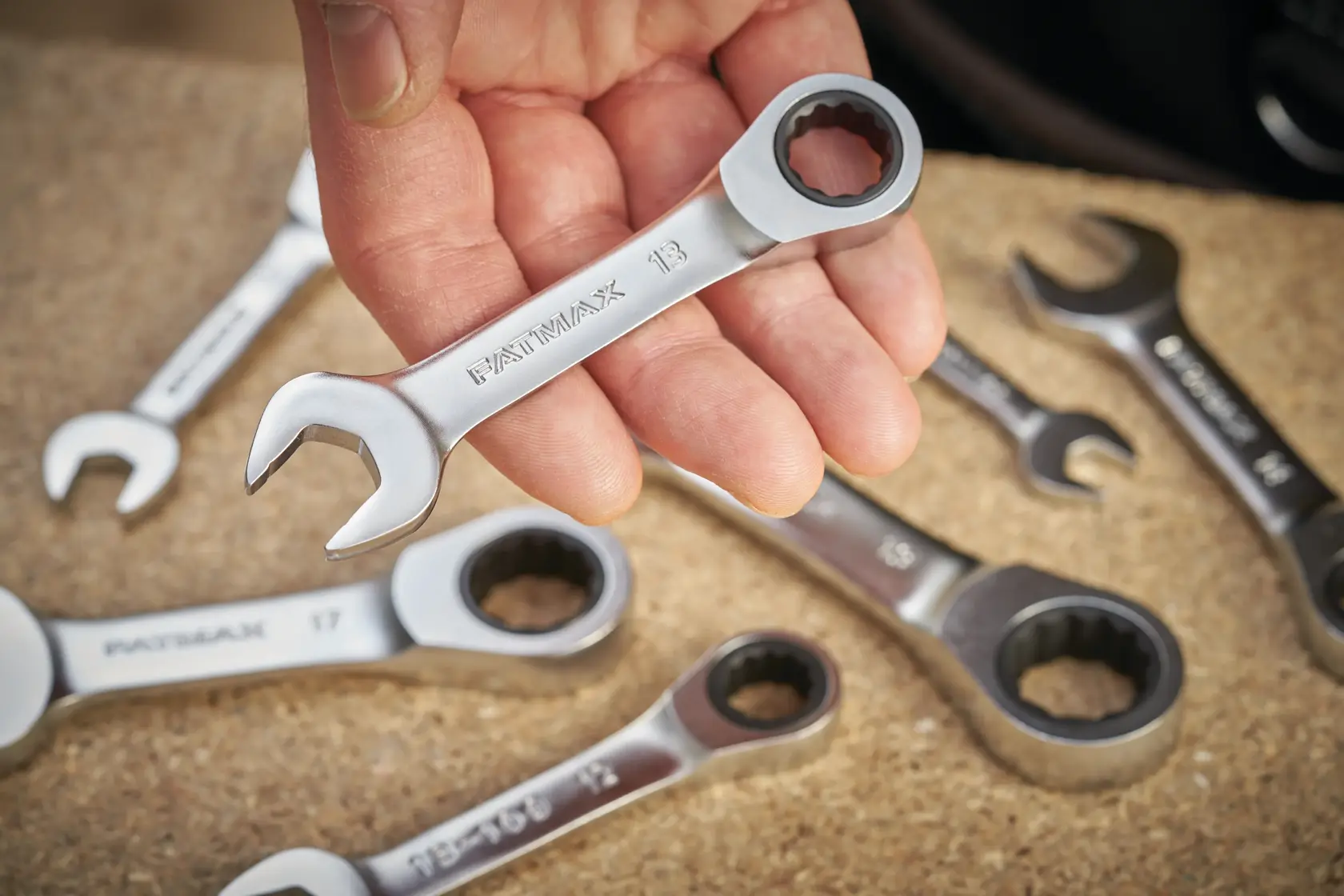 STANLEY FMMT13111-0 ratcheting combination wrench set, close-up of one wrench held in hand, others on work surface.