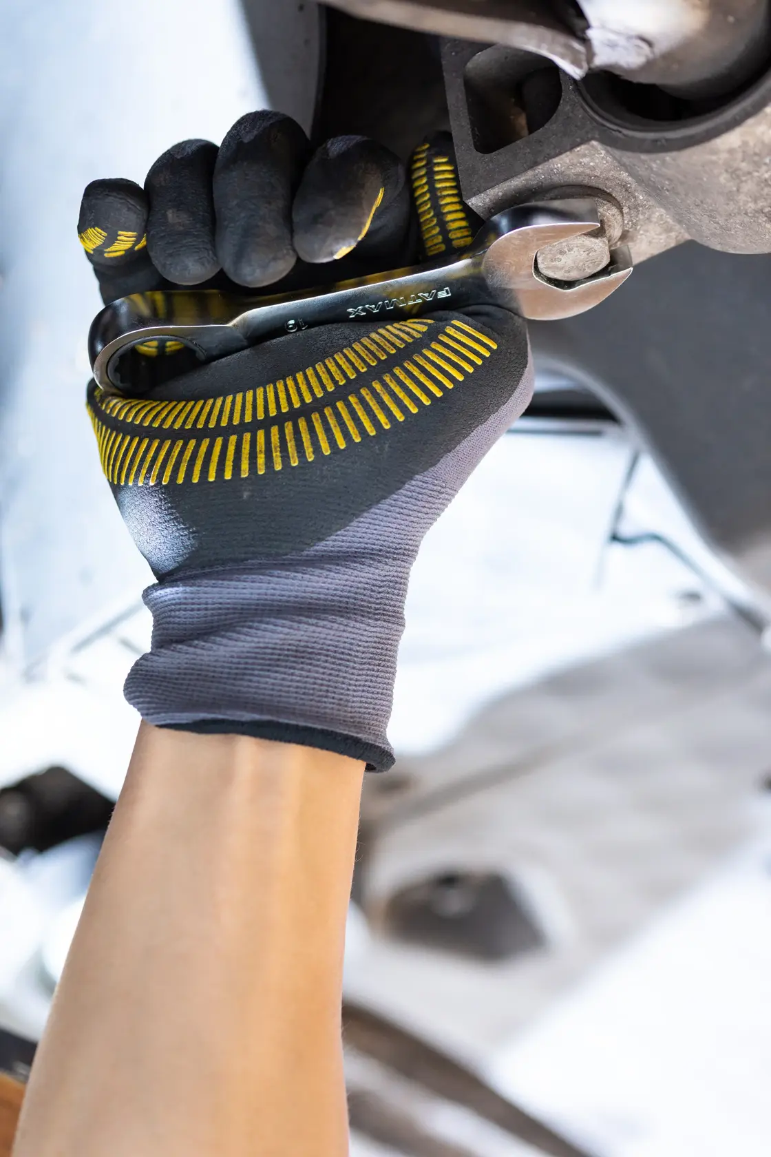 Photo of STANLEY FMMT13111-0 mechanic using wrench, wearing black and yellow gloves, close-up view.